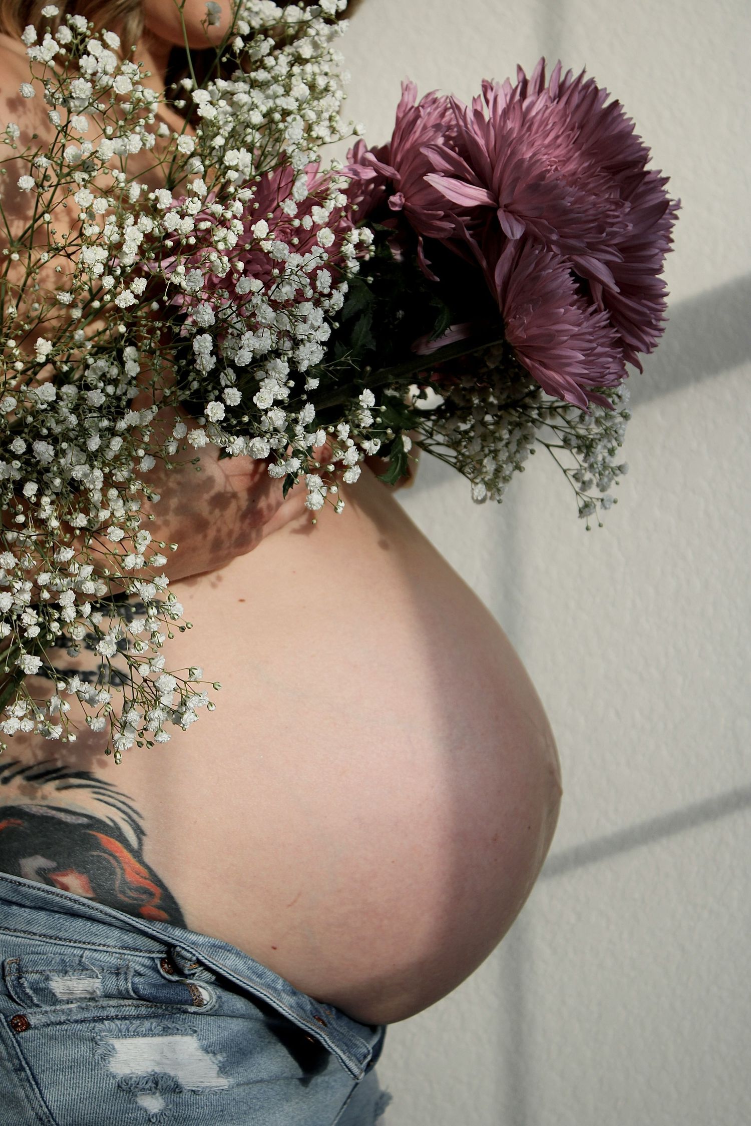 Close-up of pregnant belly with purple and white flowers in natural light.