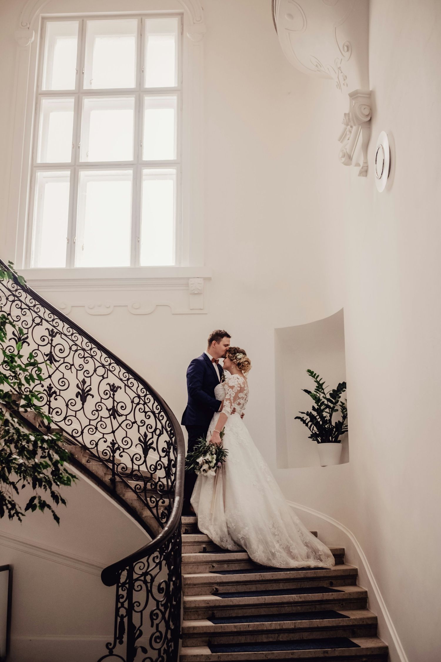 Bride and groom share a romantic moment on an elegant curved staircase with ornate iron railings.