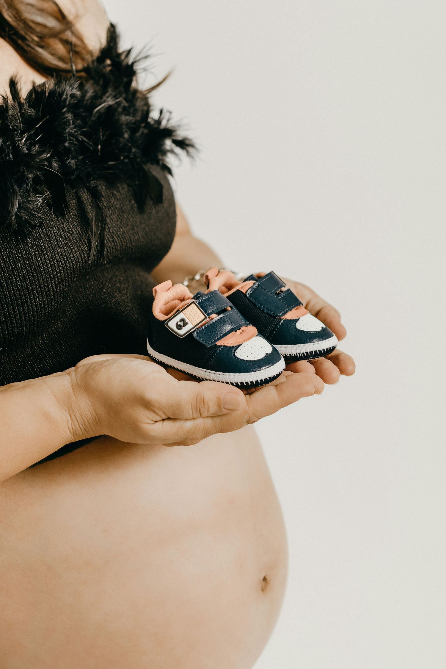 Close-up of pregnant woman holding small navy blue baby shoes near her bare belly.