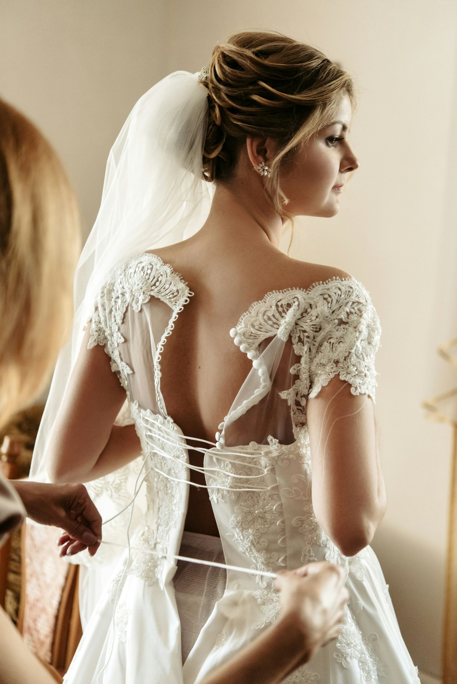 Bridesmaid lacing up intricate lace corset back of bride's wedding gown.