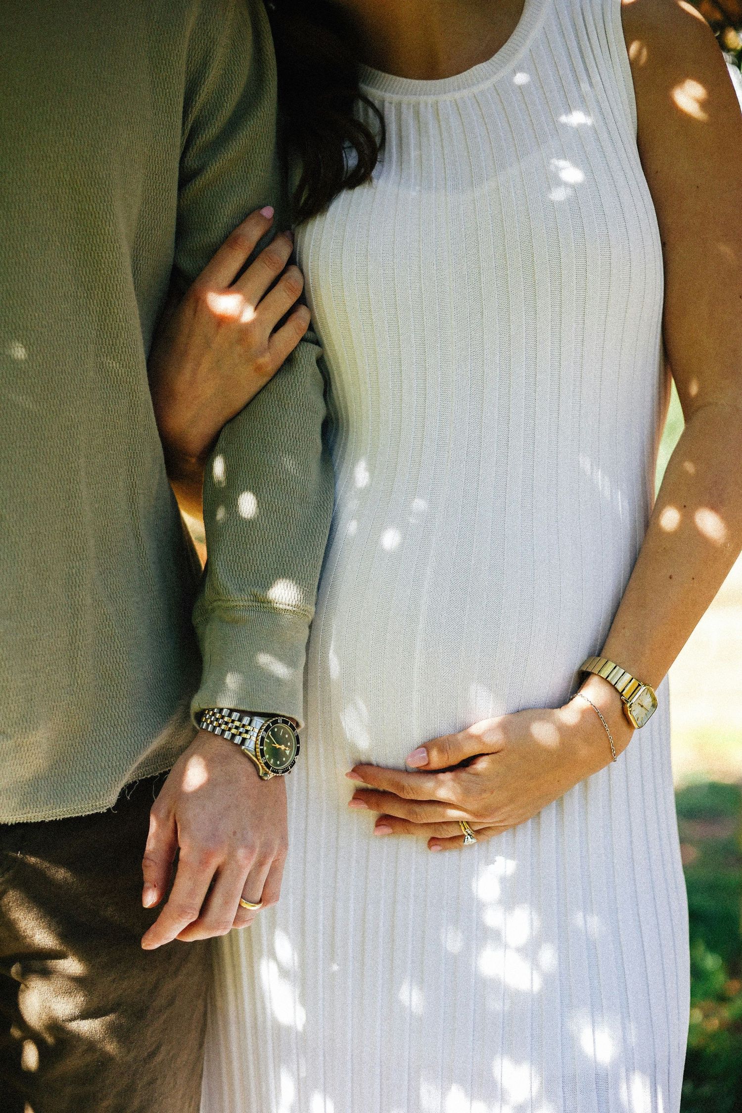 Couple embracing outdoors, woman in white ribbed dress with man's arm around her waist, both wearing watches.