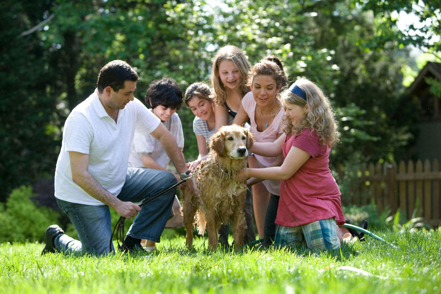 Happy family with children and a golden retriever dog playing together in a sunny green backyard.