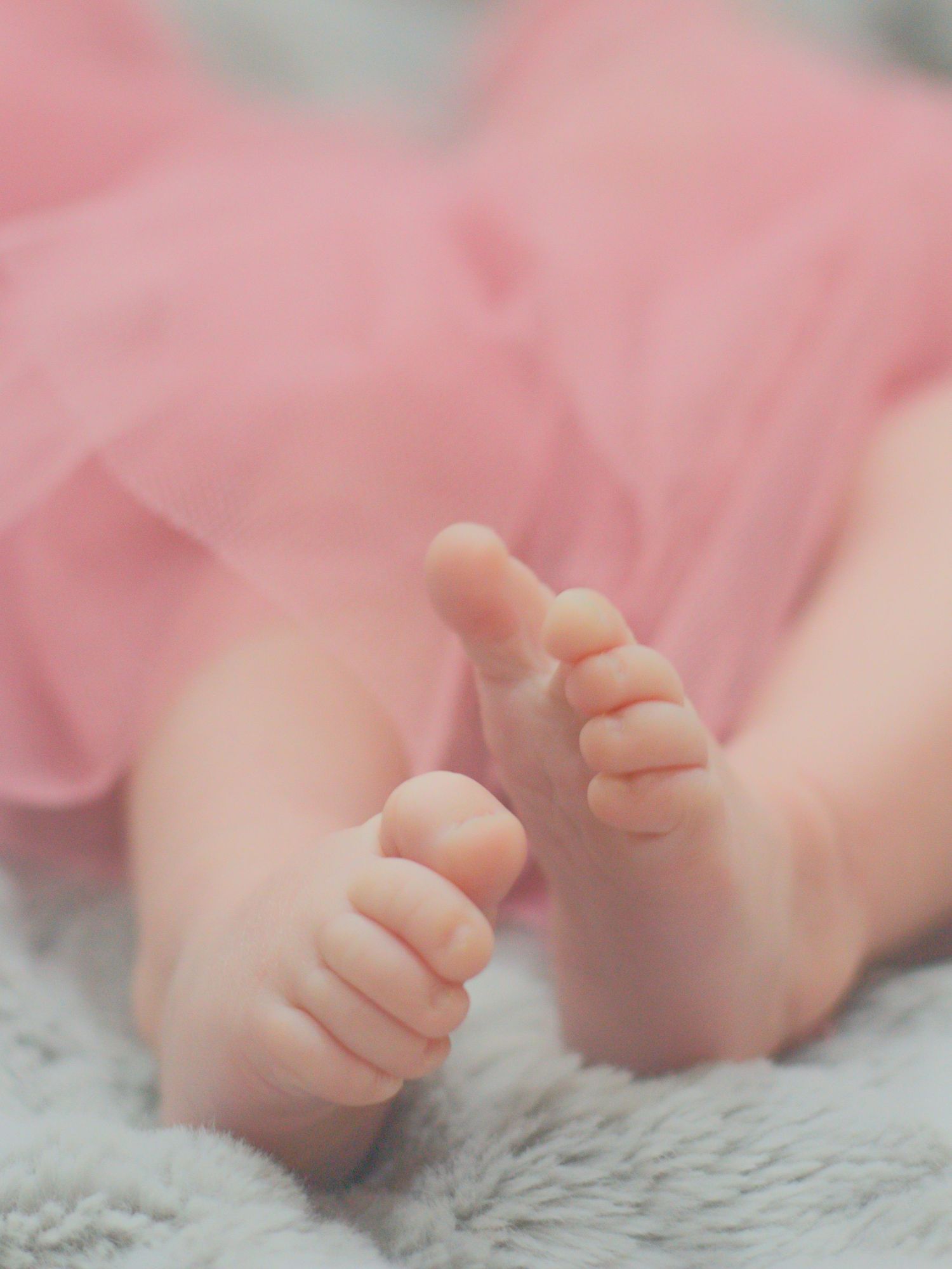 Cute newborn baby feet with pink tutu skirt on soft blanket.