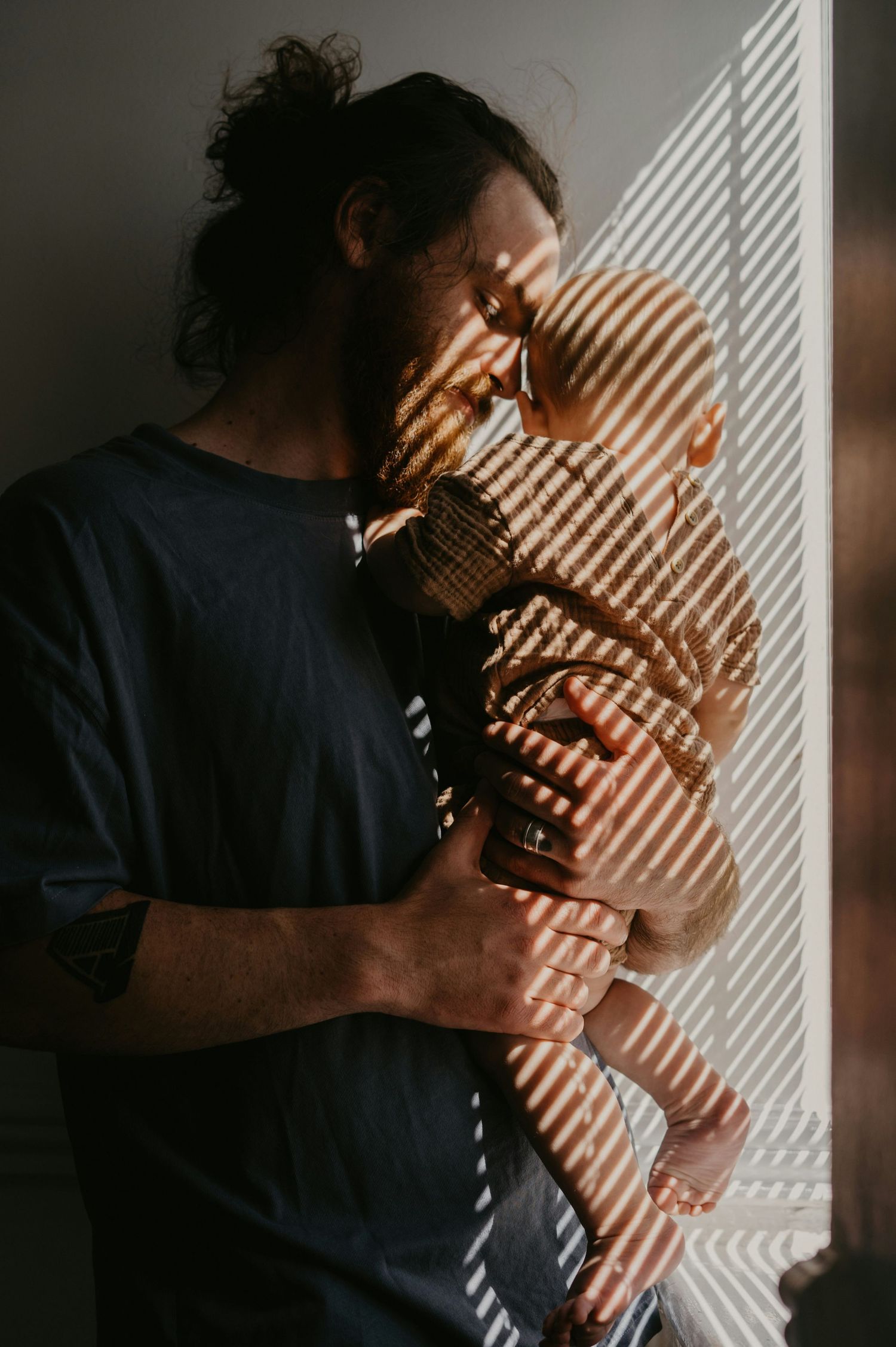 Father holding newborn baby near window with beautiful striped shadow light pattern.