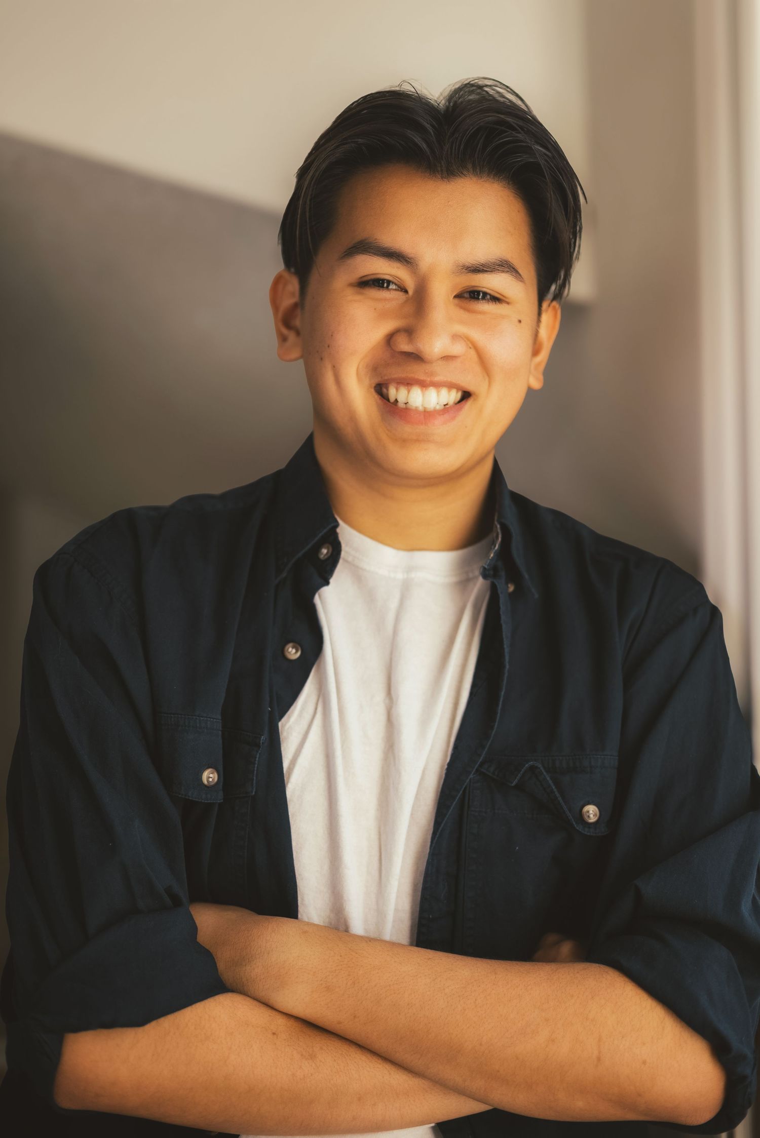 Smiling young Asian man with crossed arms wearing navy shirt indoors.