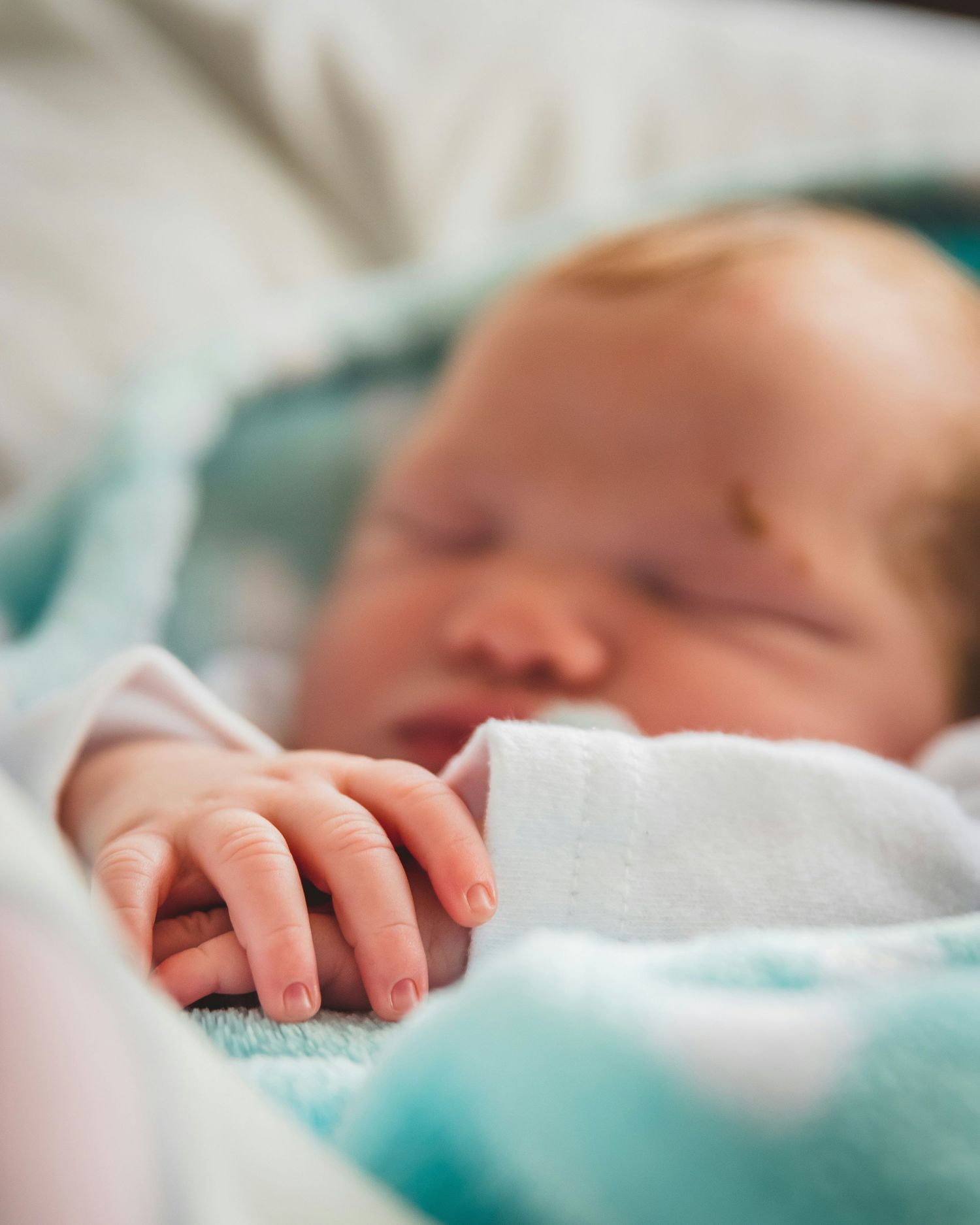 Sleeping newborn baby with red hair wrapped in teal and white blanket.