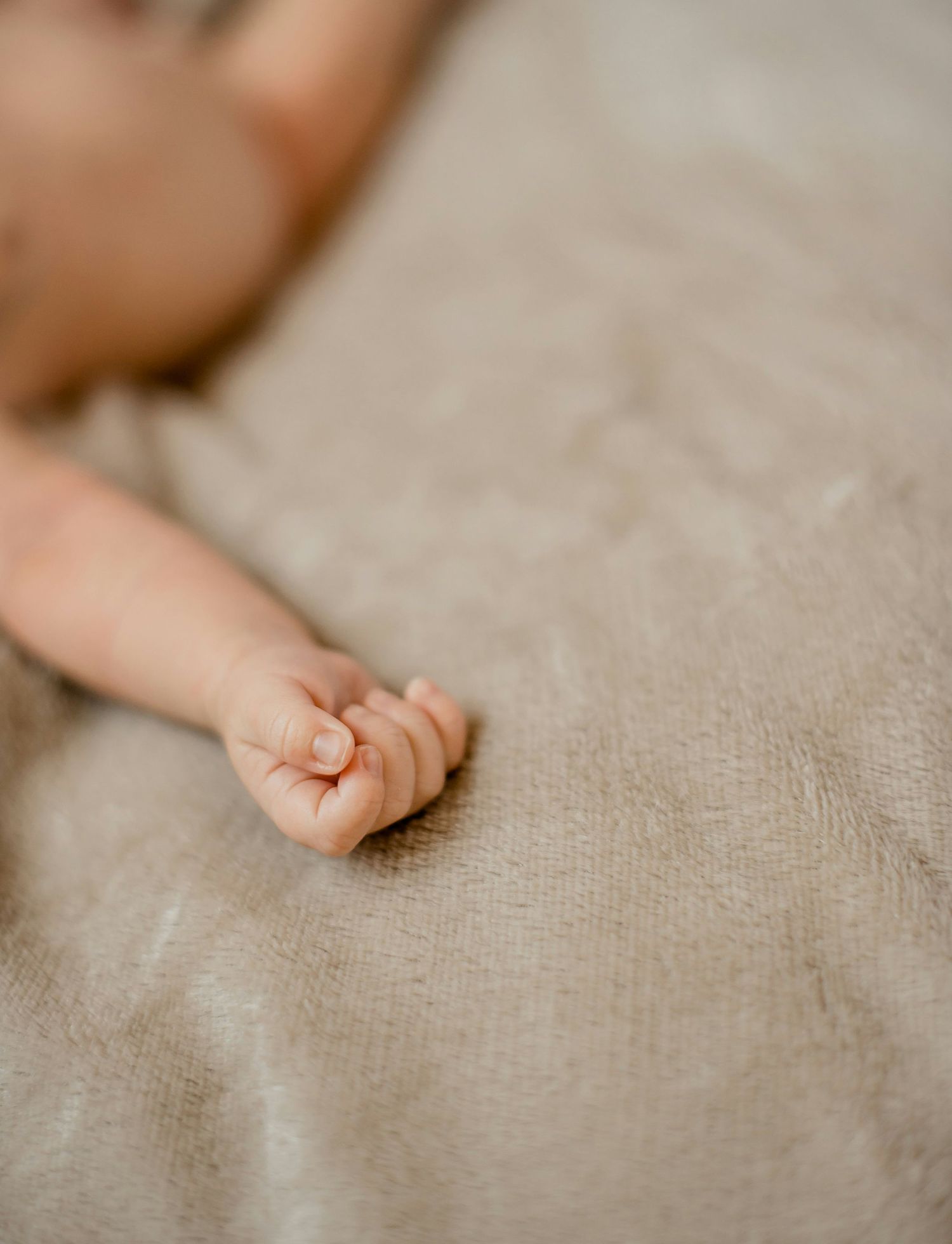 Tiny newborn baby fist resting on neutral linen fabric surface.