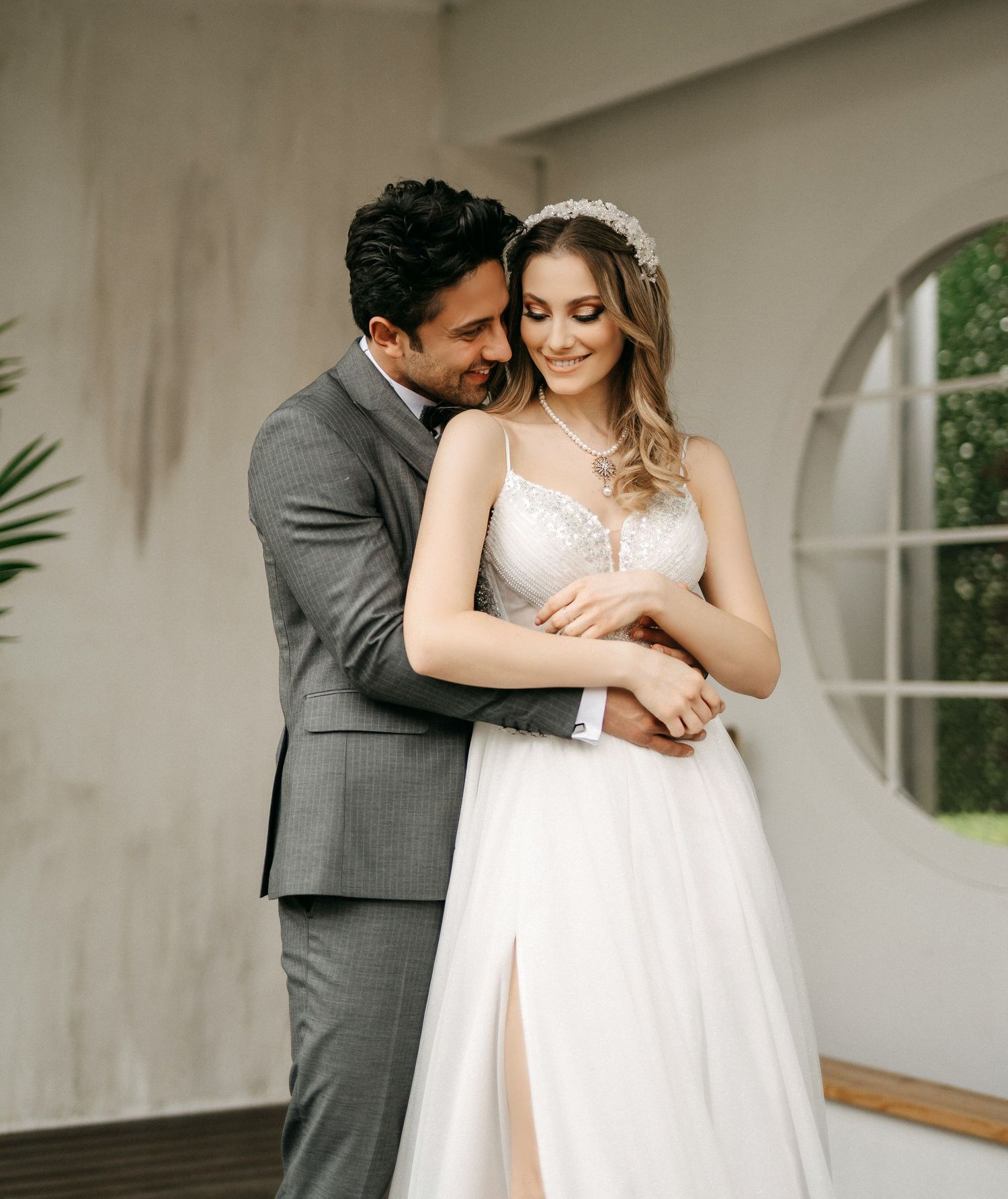 Bride and groom share a tender embrace, with groom in gray suit holding bride in lace wedding gown with tulle skirt.