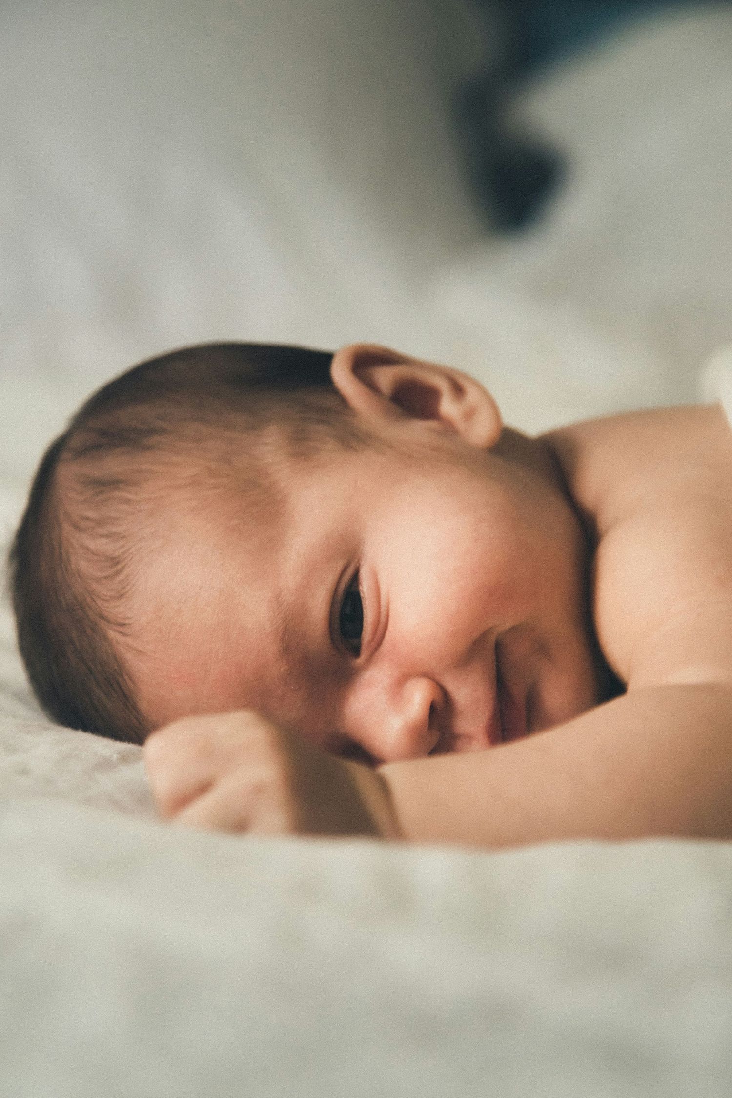 Newborn baby lying on white blanket with eyes open, peaceful close-up portrait.