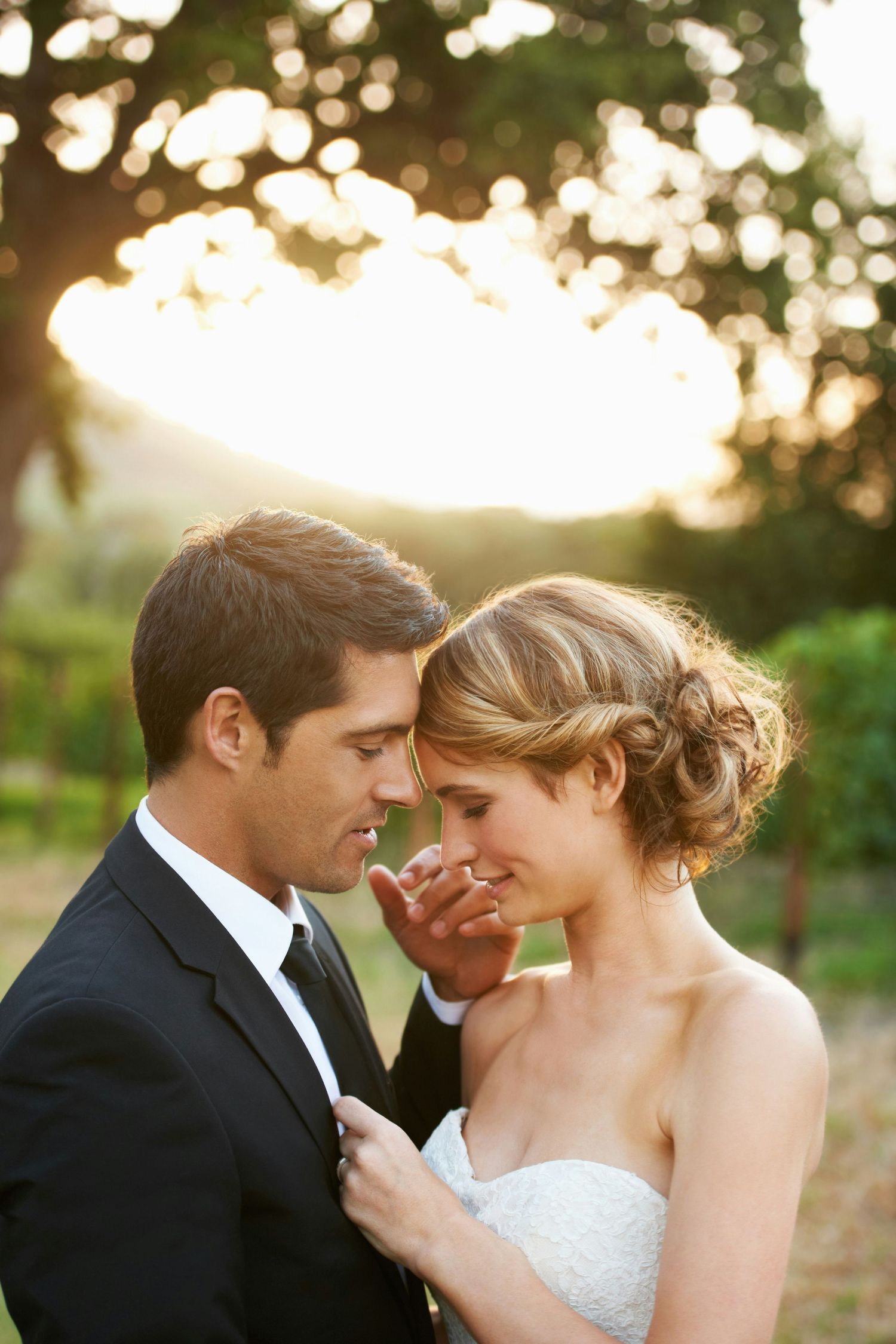 Groom tenderly cupping brides face as they share a romantic moment together in golden sunset light.