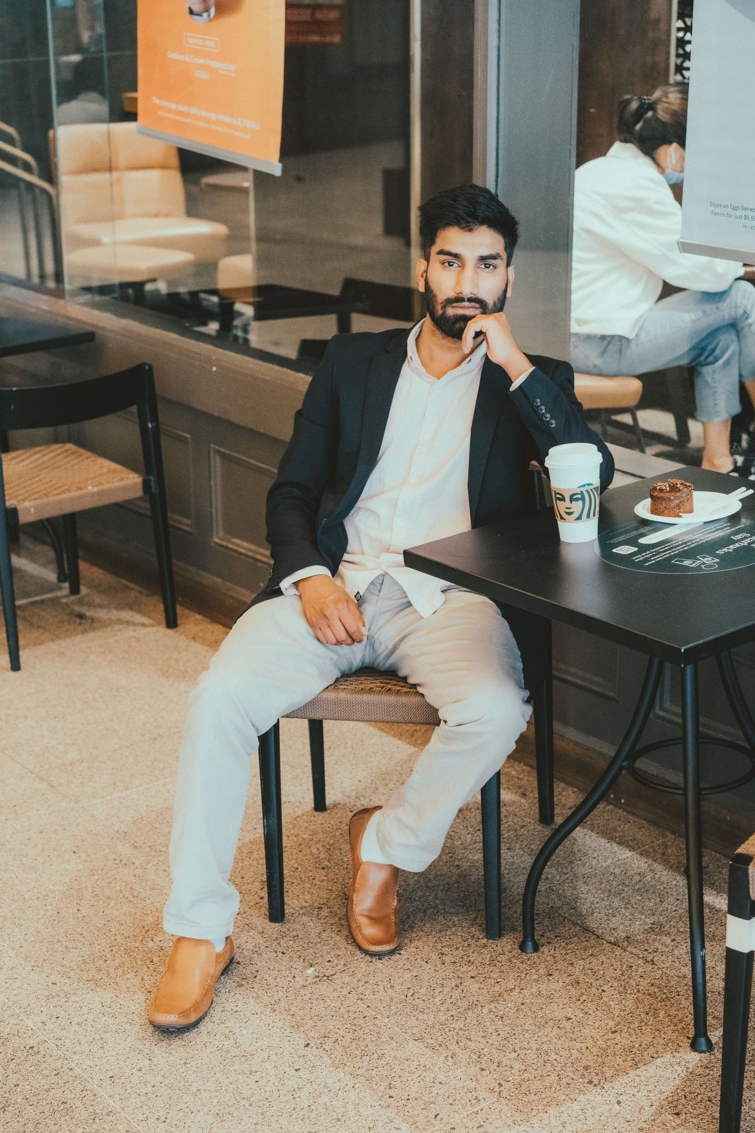 Stylish bearded man in black blazer sitting at cafe table with coffee.