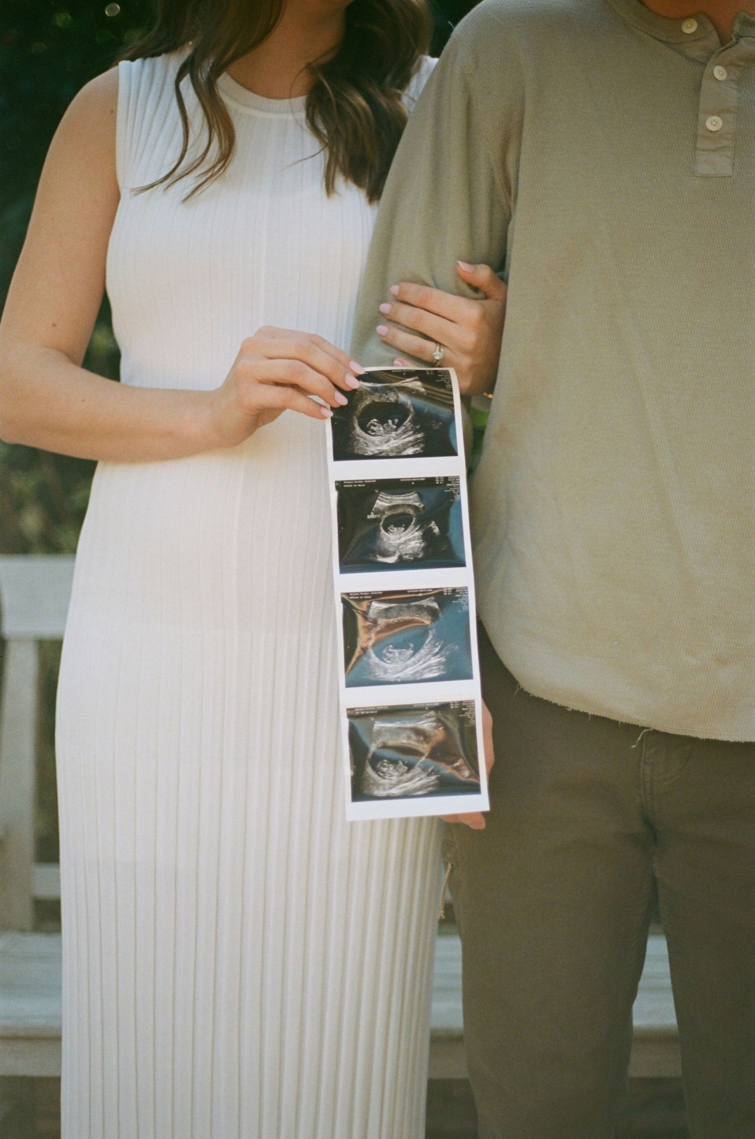 Couple holding strip of ultrasound photos during outdoor pregnancy announcement.