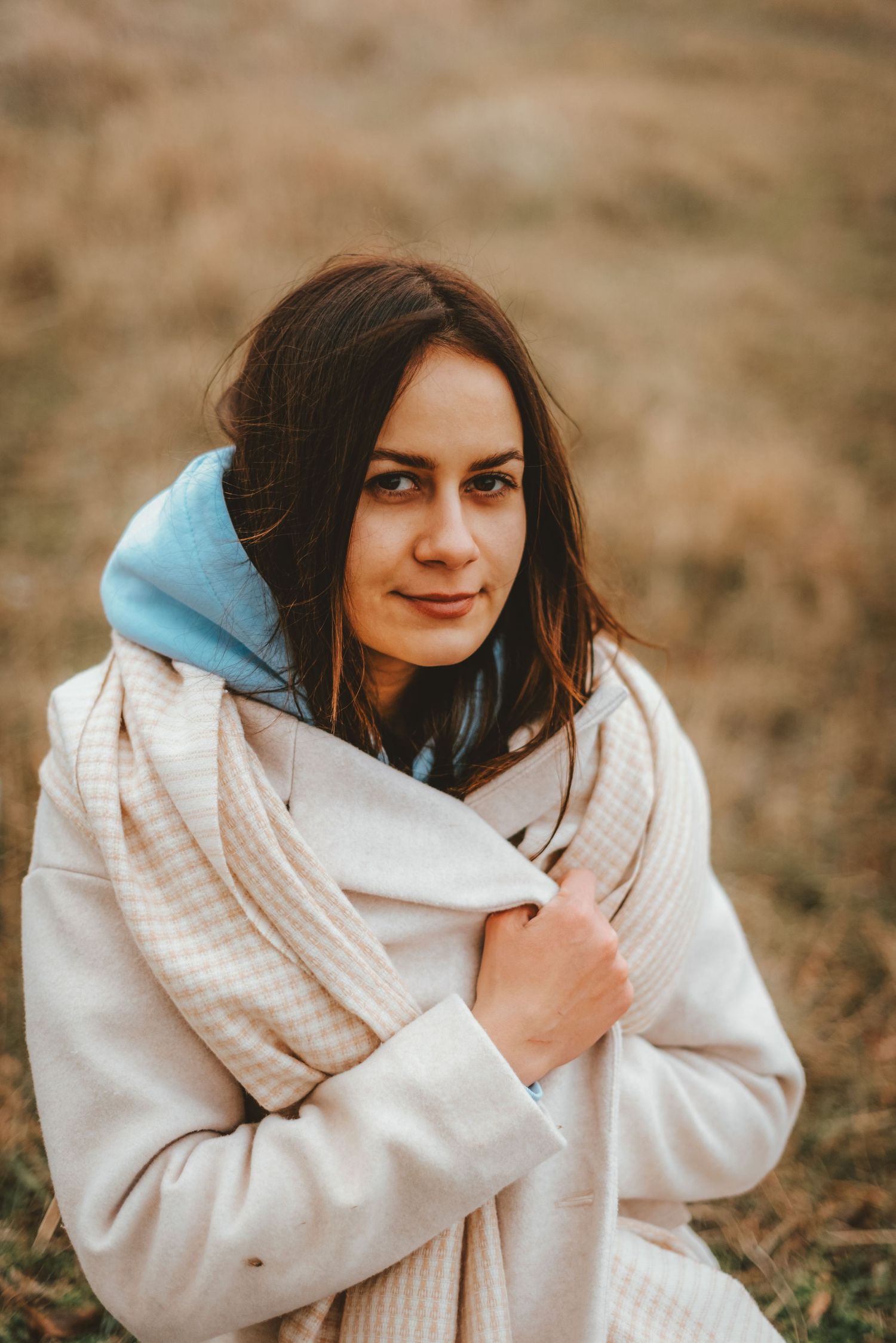 Young woman in white coat and scarf smiling outdoors in autumn field.