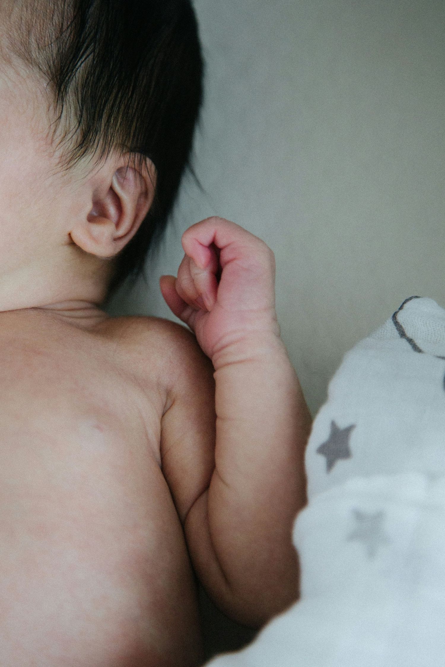 Close-up of sleeping newborn baby ear and tiny hand next to star-print toy.