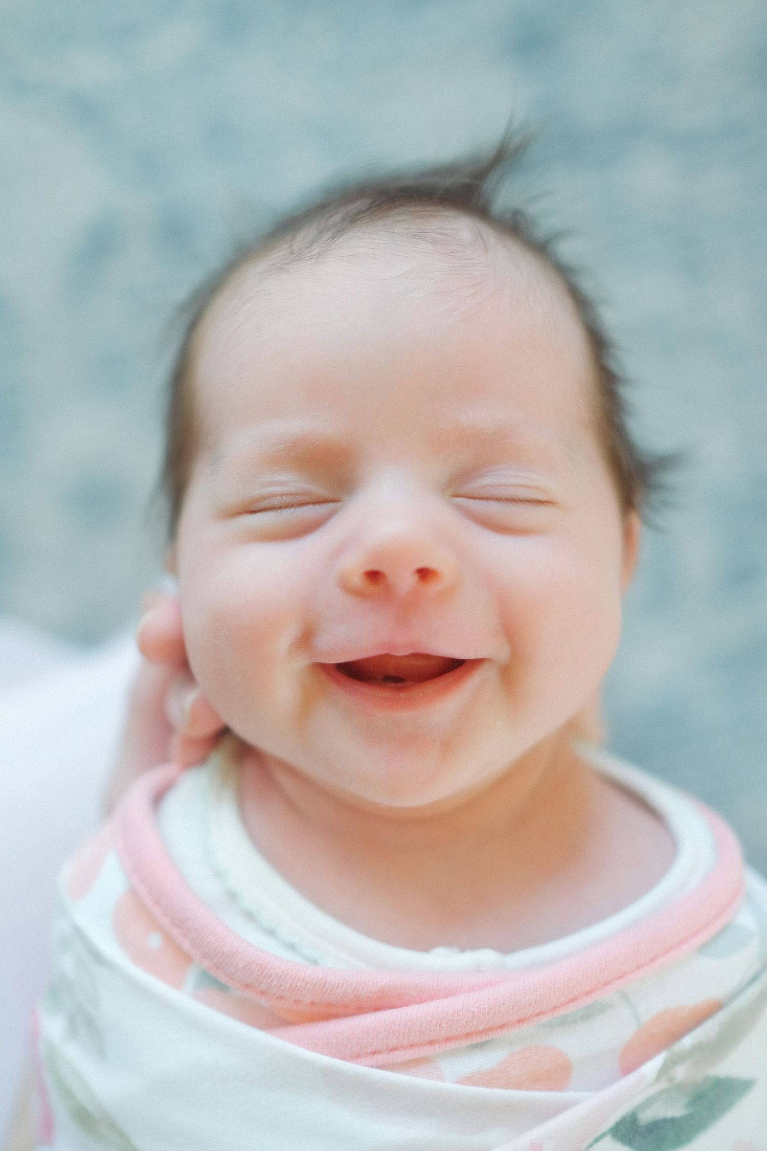 Close-up of smiling newborn baby swaddled in colorful blanket with eyes closed.