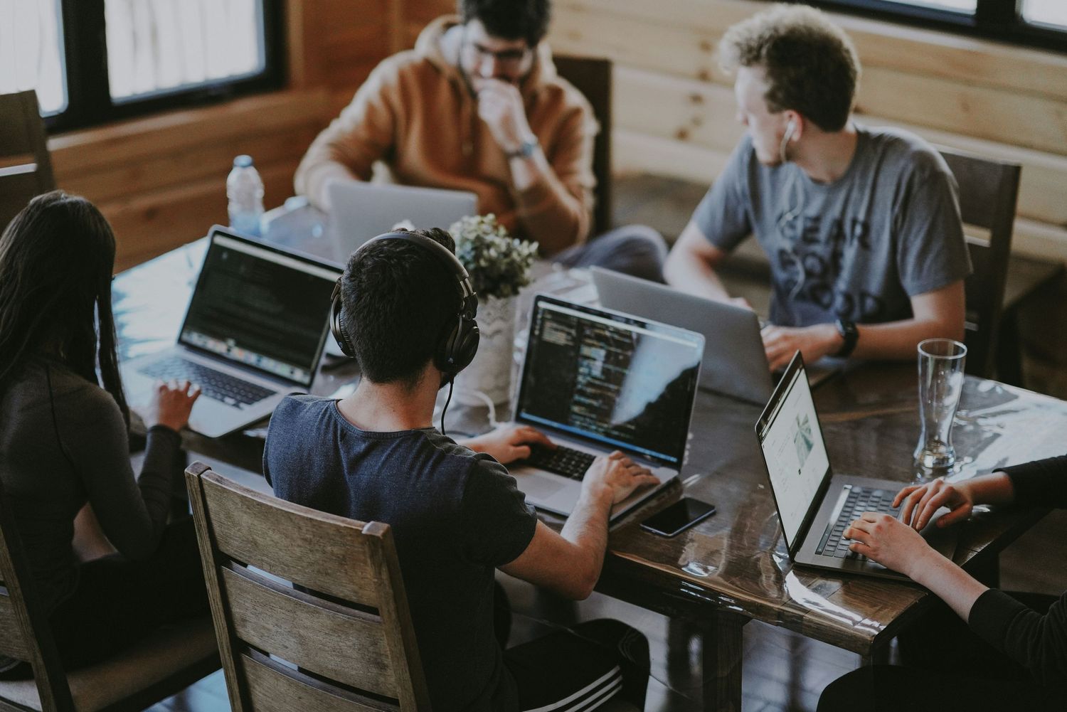 Group of young professionals collaborating on laptops at a wooden table in a modern co-working space.