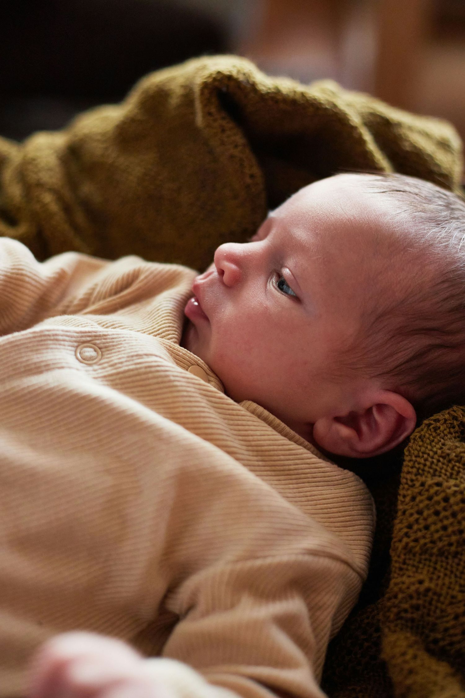 Close-up of a newborn baby in a beige striped onesie gazing upward while resting.
