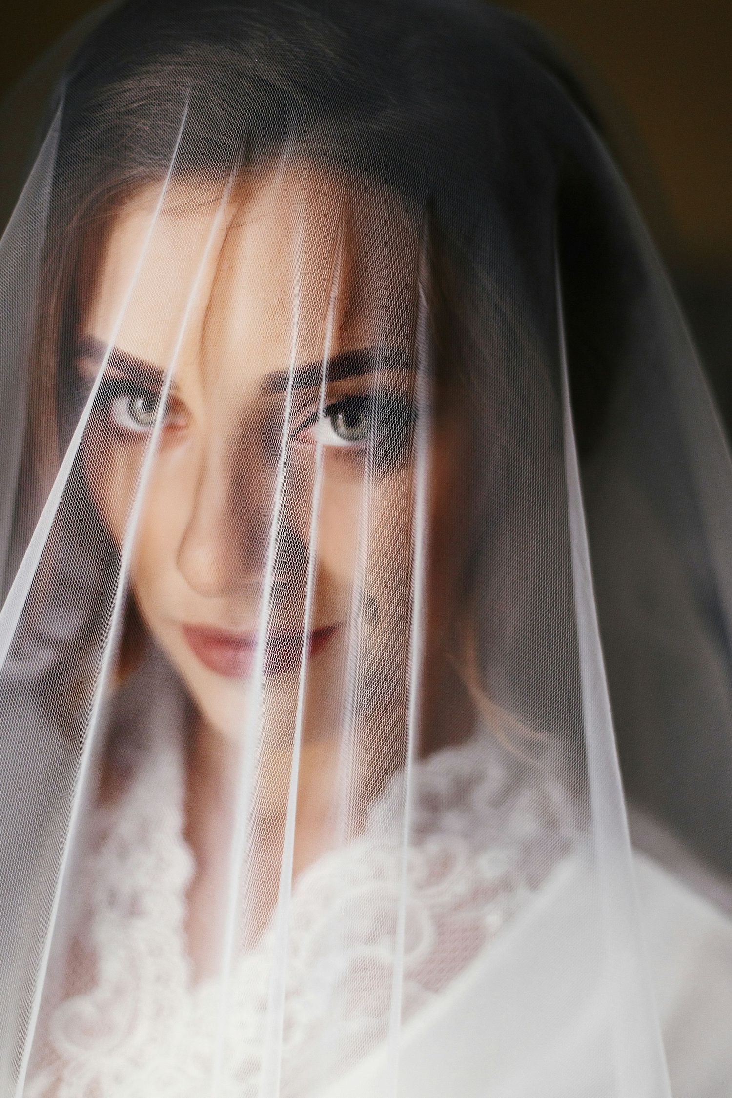 Close-up portrait of bride with smoky eyes gazing through sheer white veil.