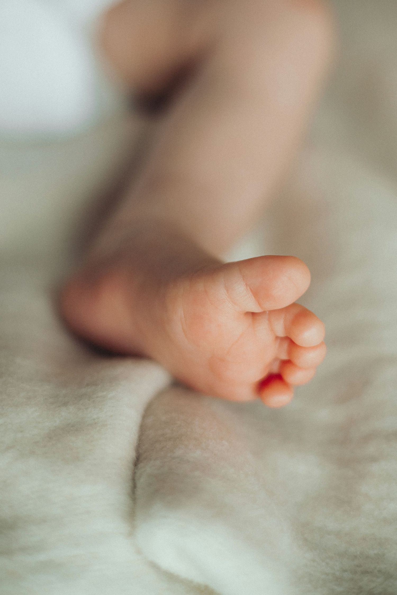 Soft focus close-up of a tiny newborn baby foot on a white blanket.