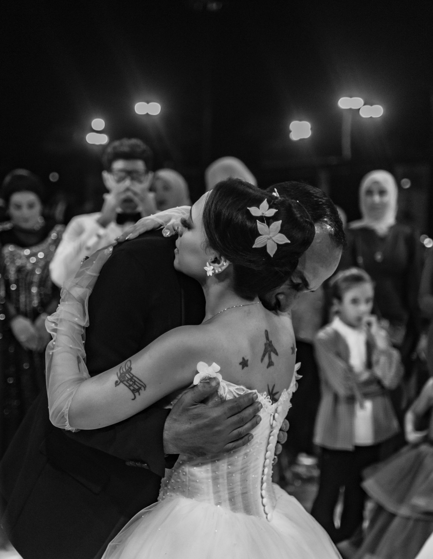 Bride and groom share their first dance in a black and white photo, surrounded by wedding guests and soft lights.