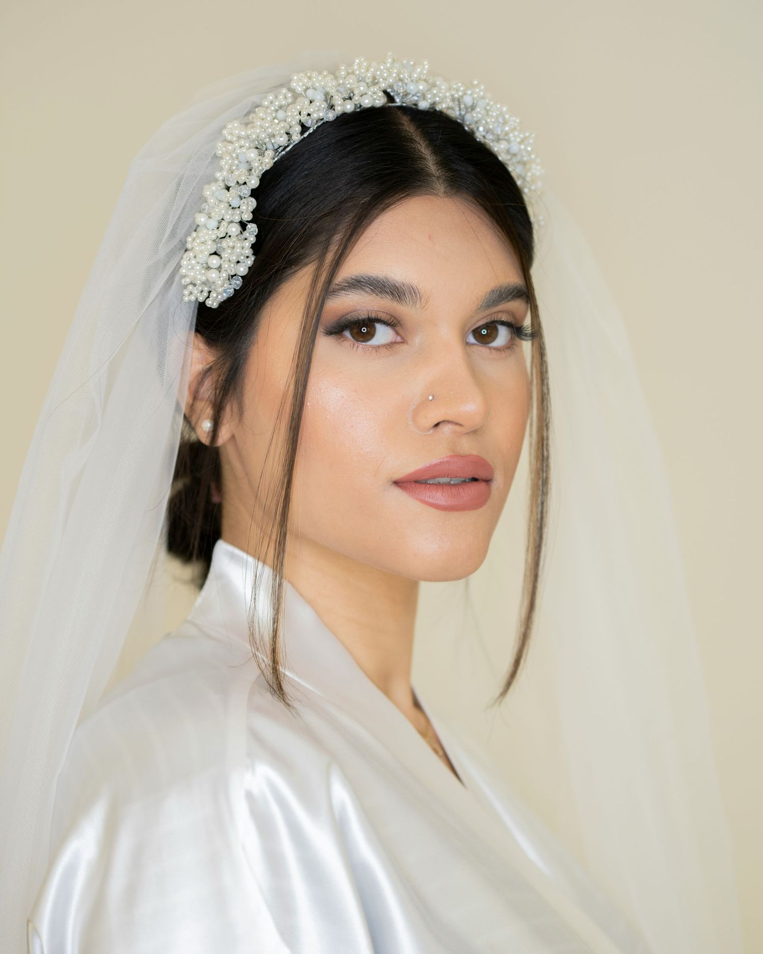 Bride wearing a pearl-adorned headband with white veil and natural makeup portrait.