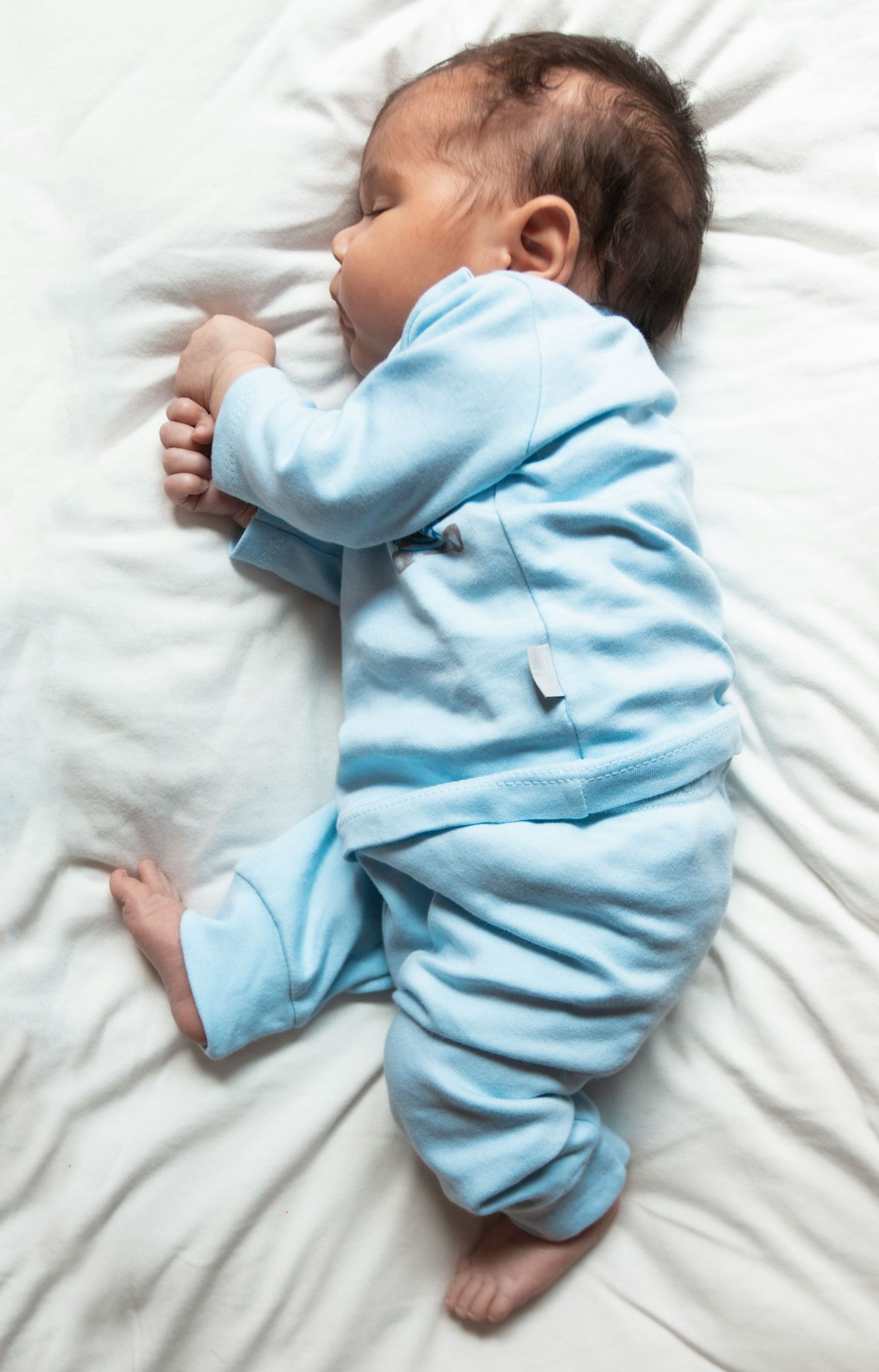 Sleeping newborn baby in a light blue striped footie pajama lying on white bedding.