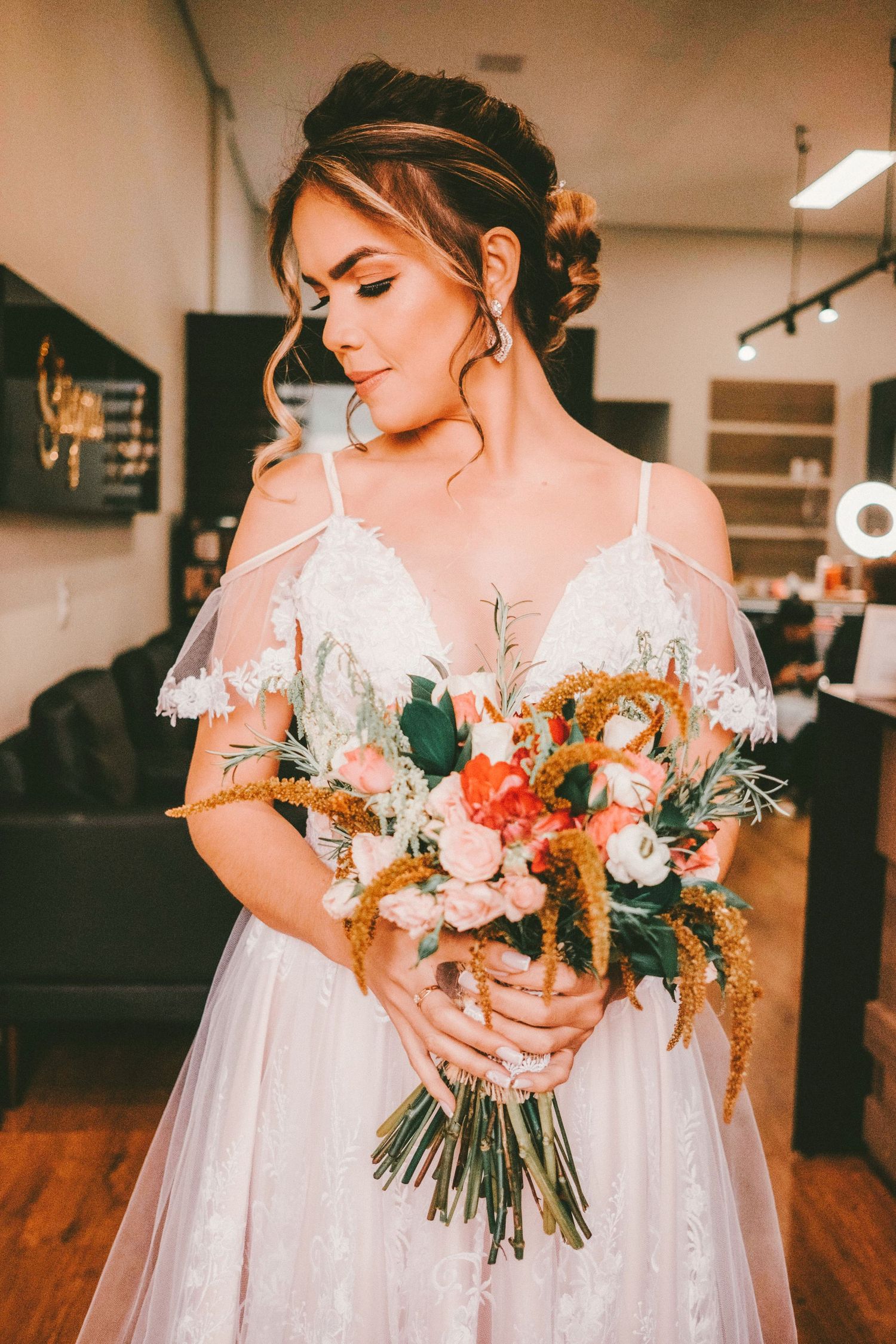 Bride in white off-shoulder gown holding a colorful bouquet of pink and coral flowers in a salon.