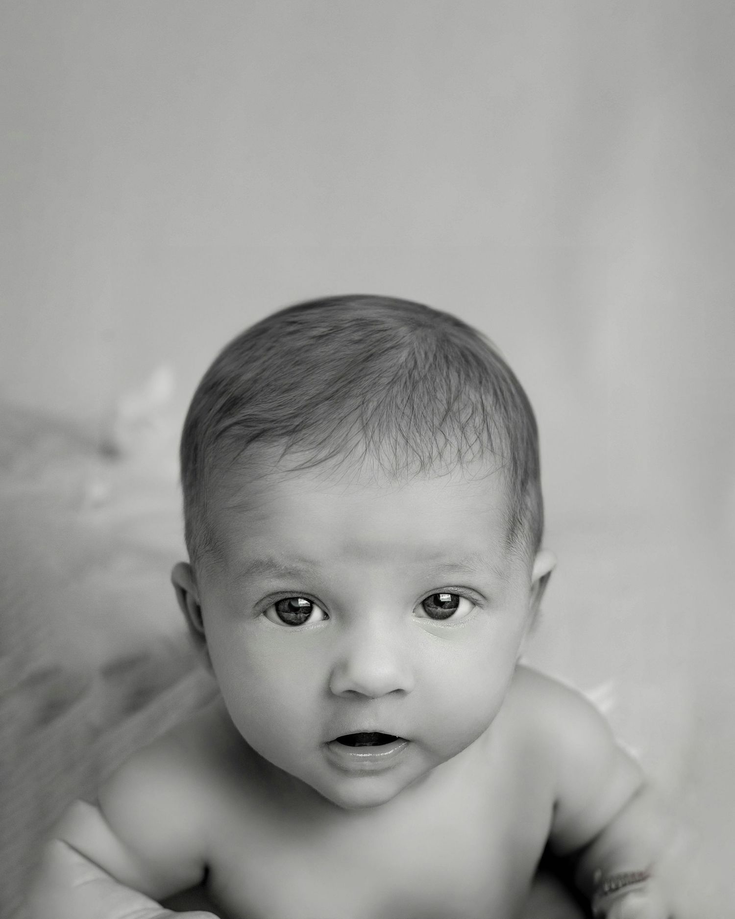 Black and white portrait of alert newborn baby during tummy time looking at camera.
