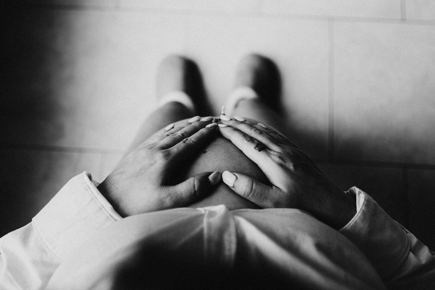 Black and white image of a person sitting on floor with hands clasped over their knees.