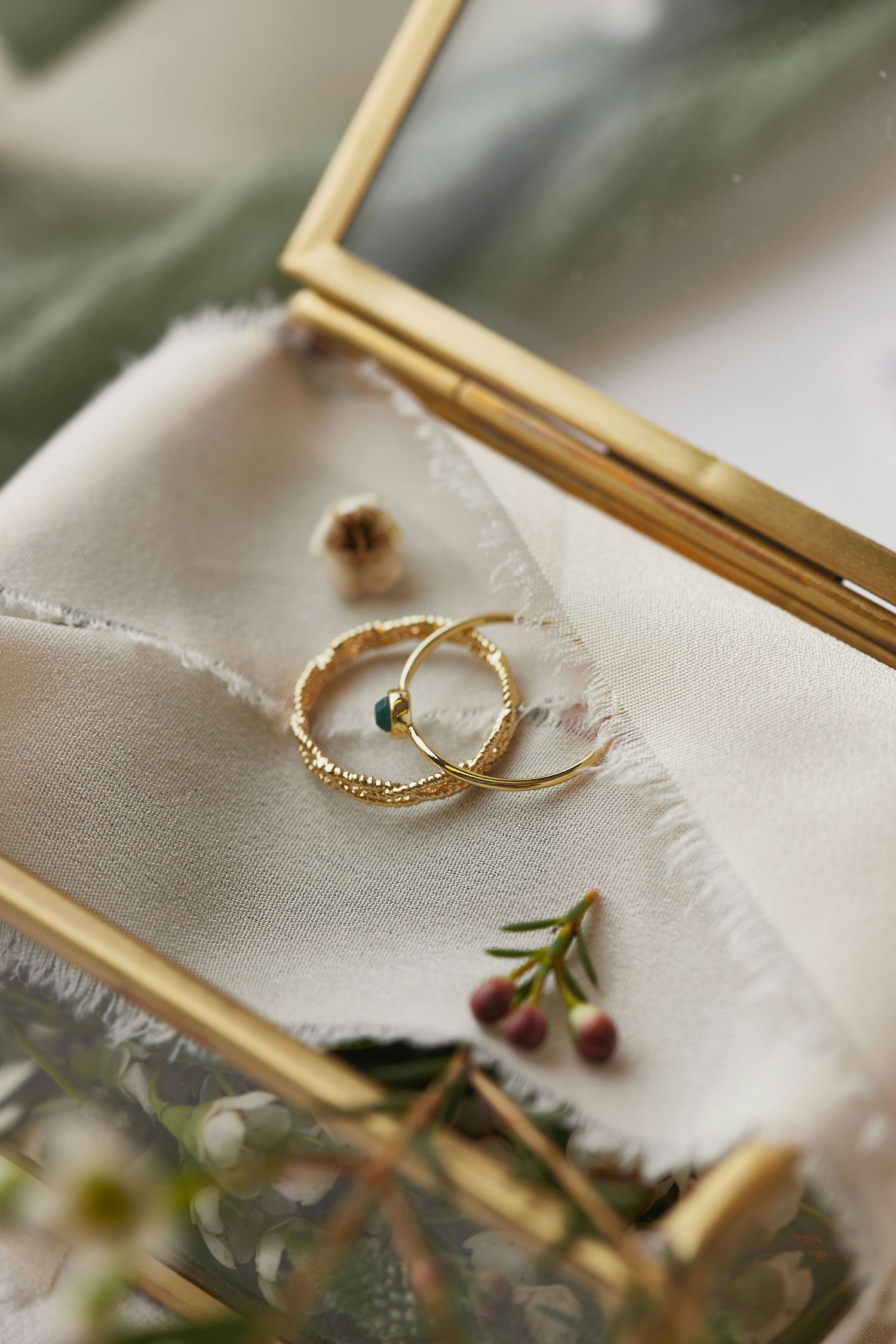 Gold hoop earrings with emerald detail displayed on white silk fabric in a gold glass jewelry box with flowers.