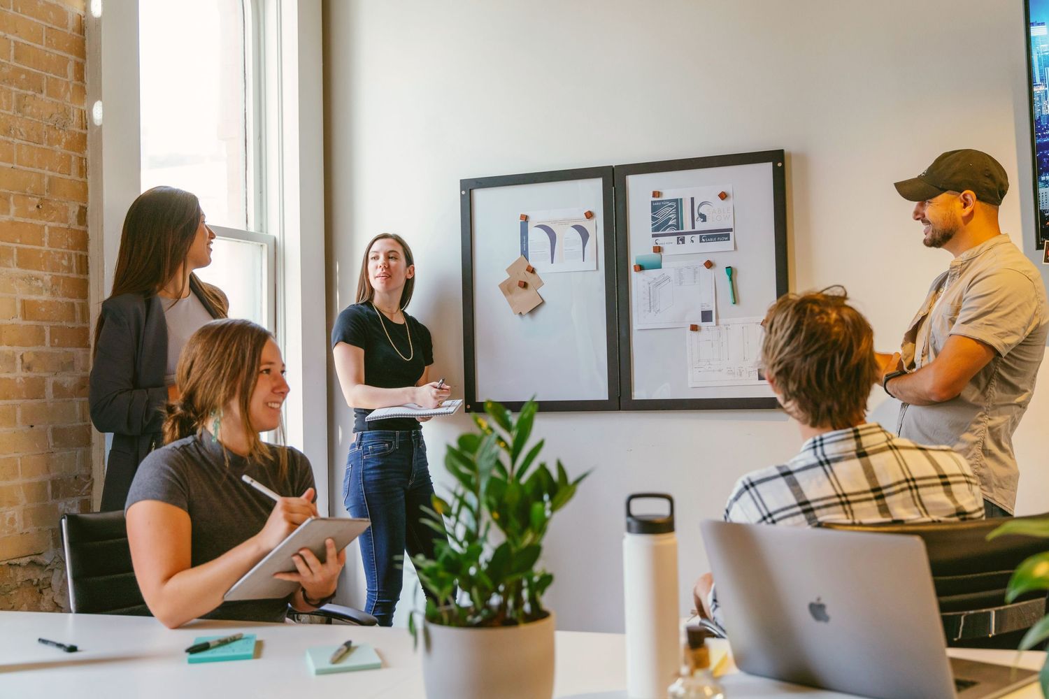 Team members collaborate in a modern office meeting room, discussing project designs displayed on a wall.