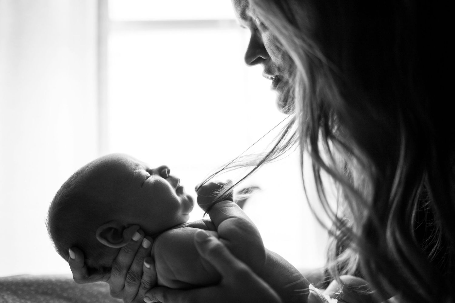 A black and white close-up of a mother tenderly smiling at her newborn baby in soft natural light.