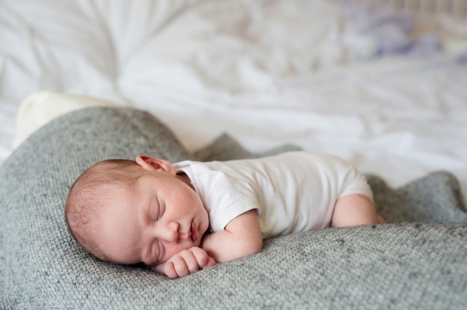 Newborn baby sleeping peacefully on a soft gray blanket in a cozy white bed.
