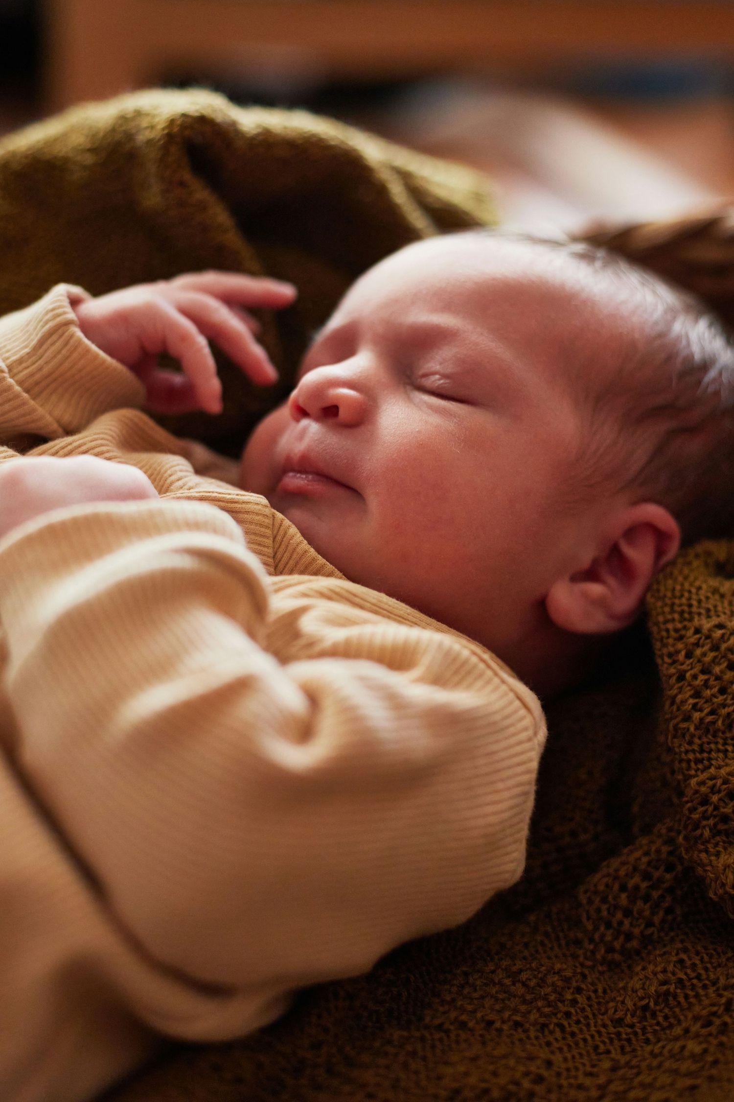 Sleeping newborn baby in a peach ribbed onesie resting on a dark olive green blanket.