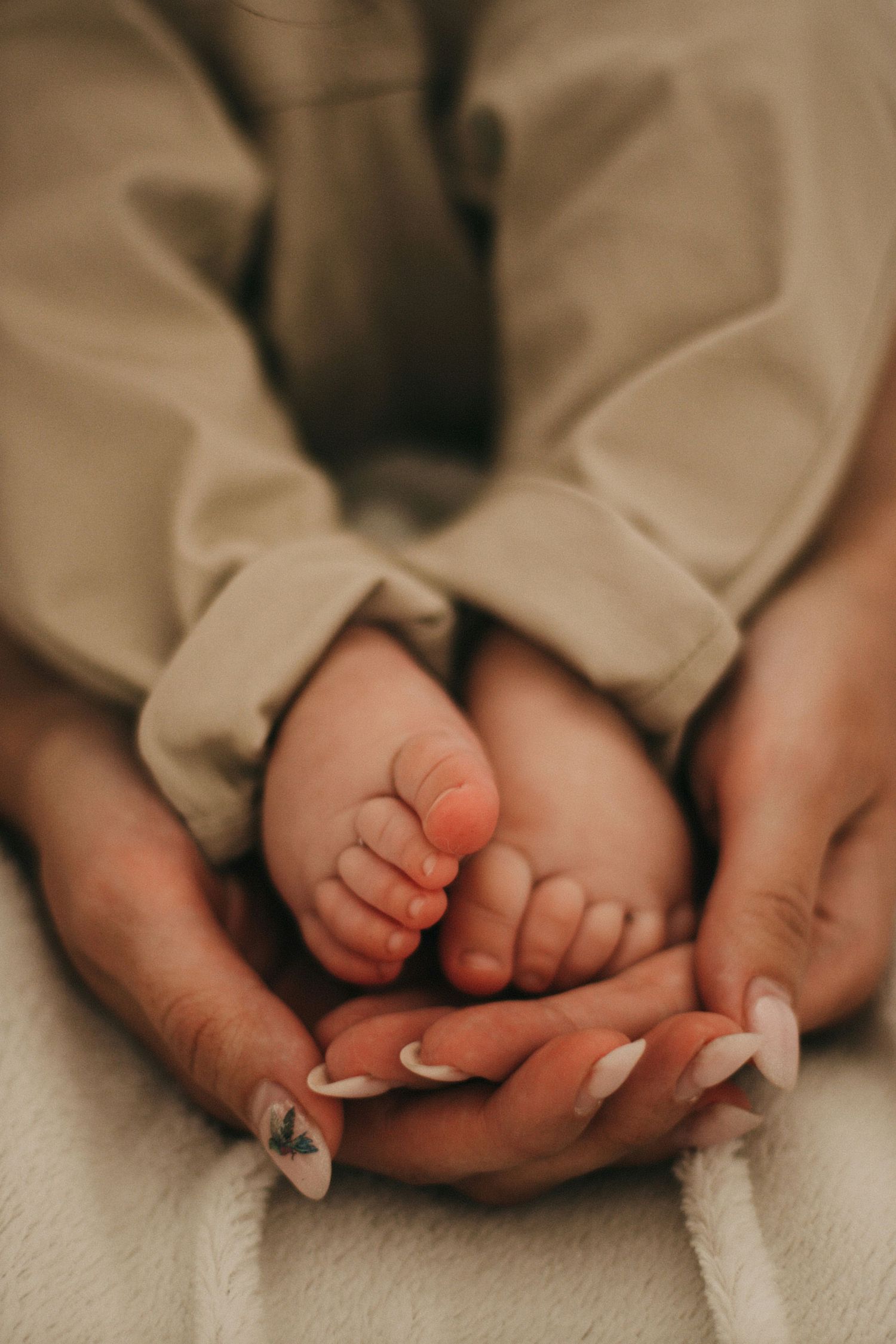 Mother with manicured nails gently cradling tiny newborn baby feet in her hands.