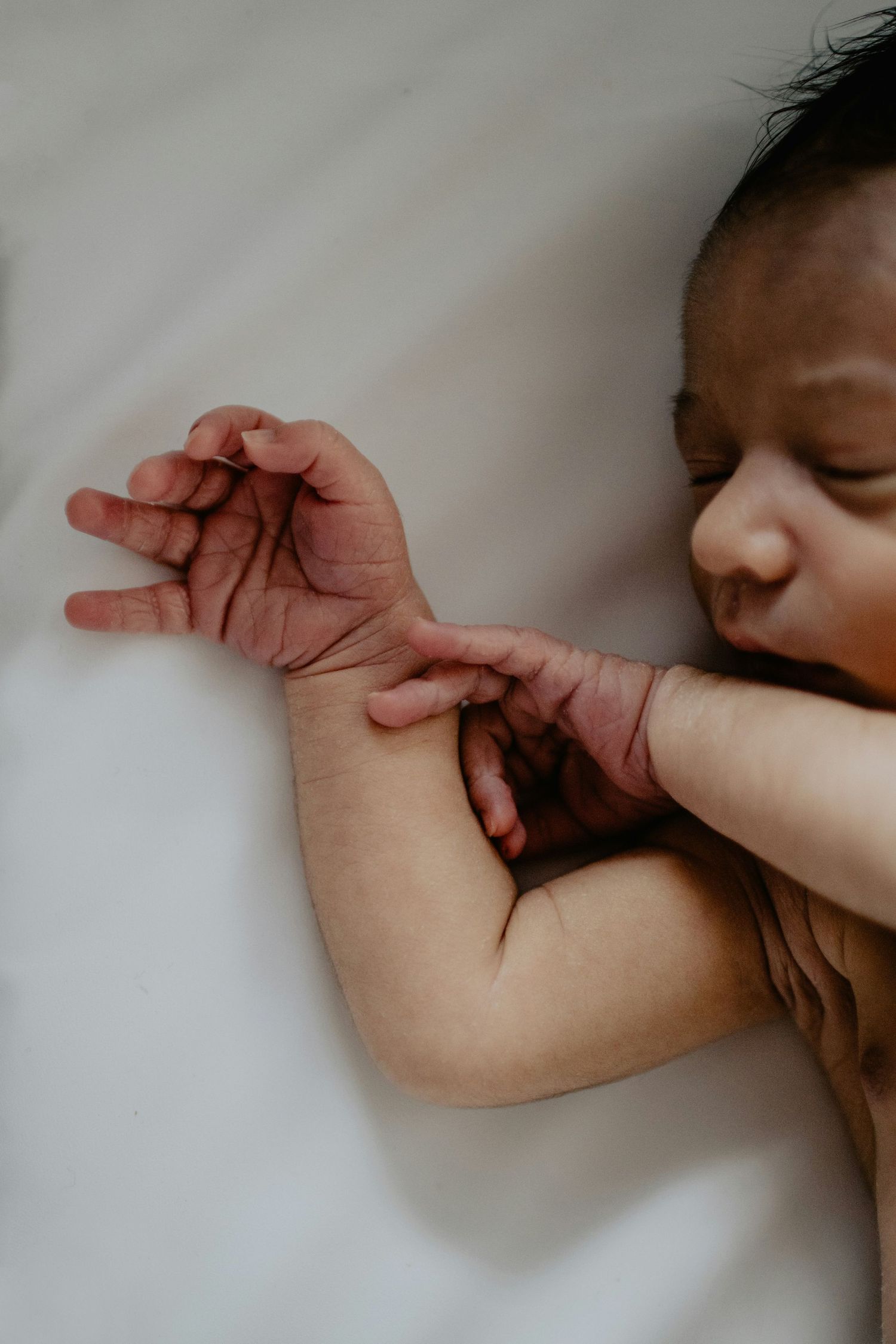 Close-up of sleeping newborn baby with tiny hands and fingers on white sheet.