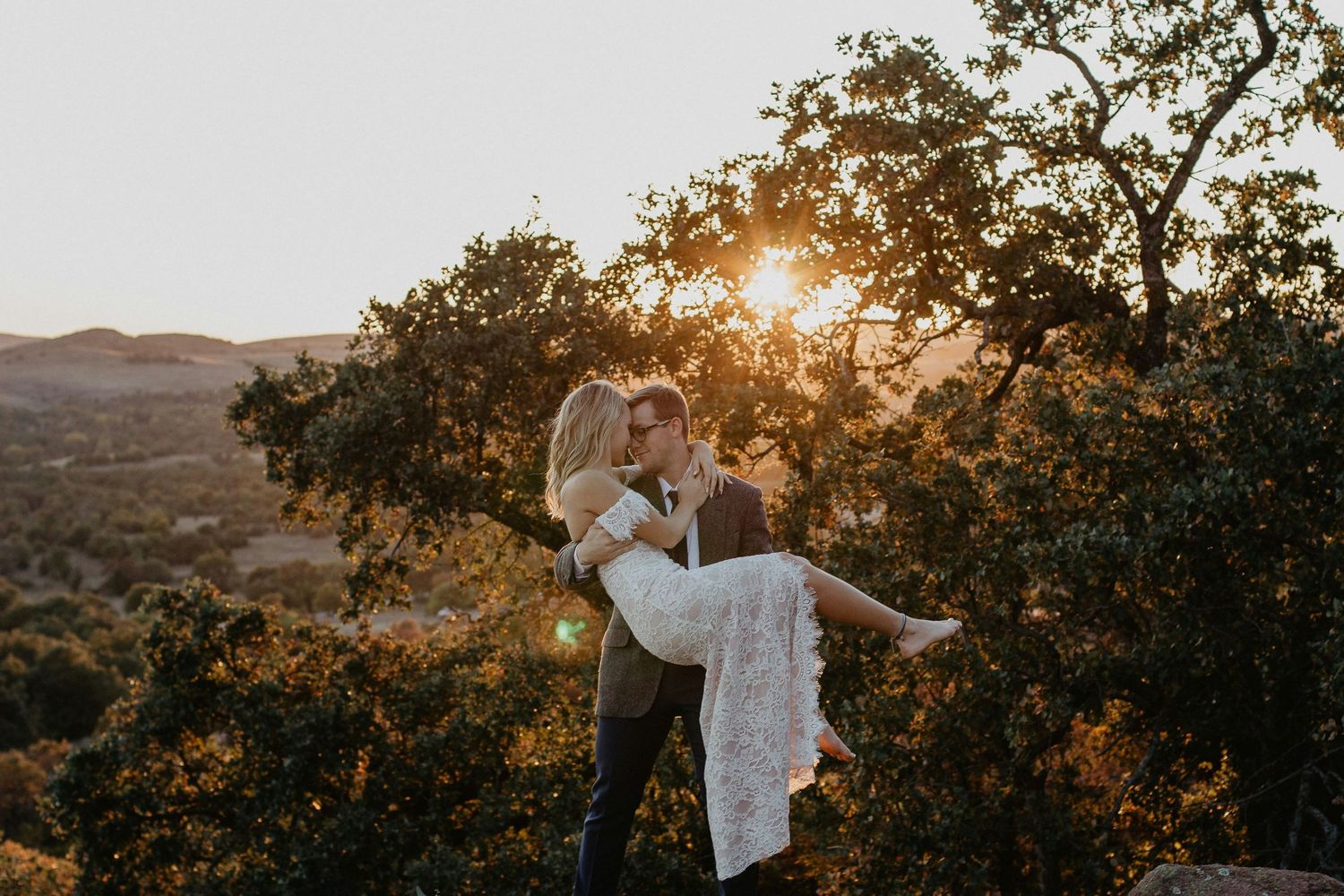 Romantic couple embracing at golden sunset with scenic mountain landscape in the background.