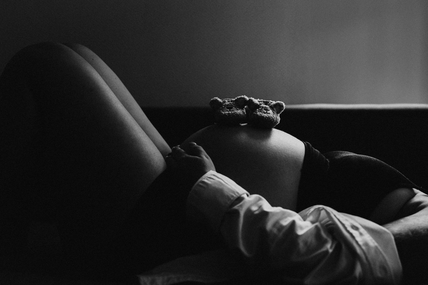 Black and white photo of pregnant woman reclining with tiny baby shoes resting on her bump.