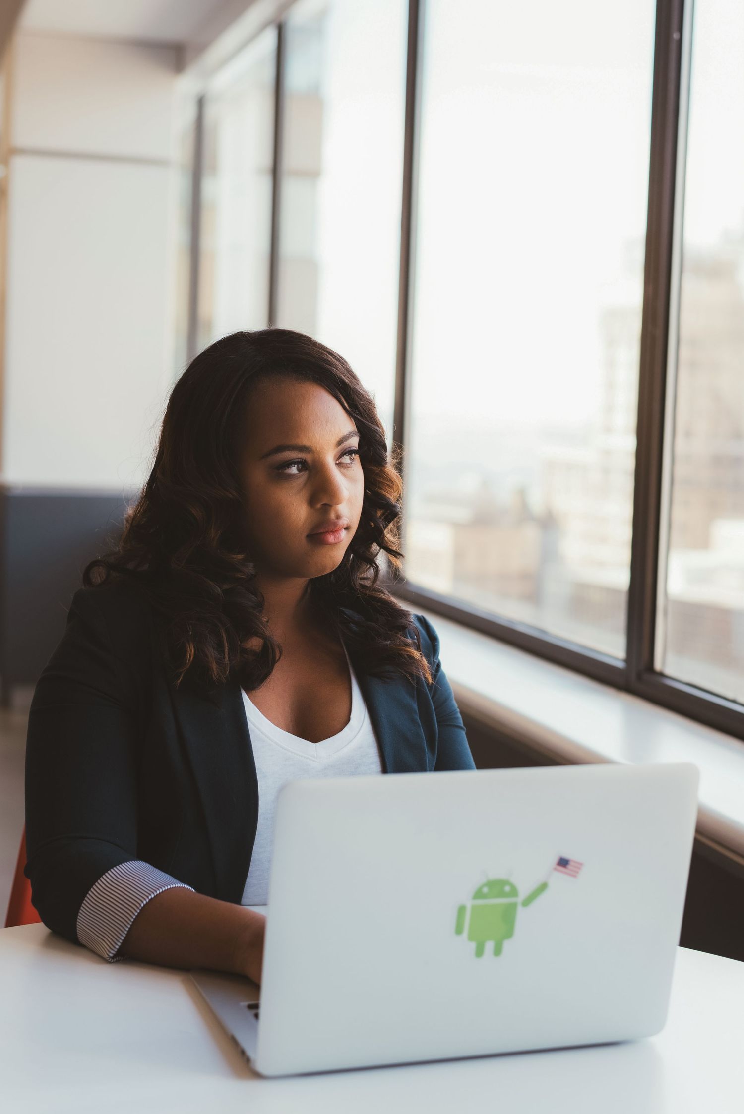 Young professional Black woman working on laptop with Android sticker in a bright modern office.