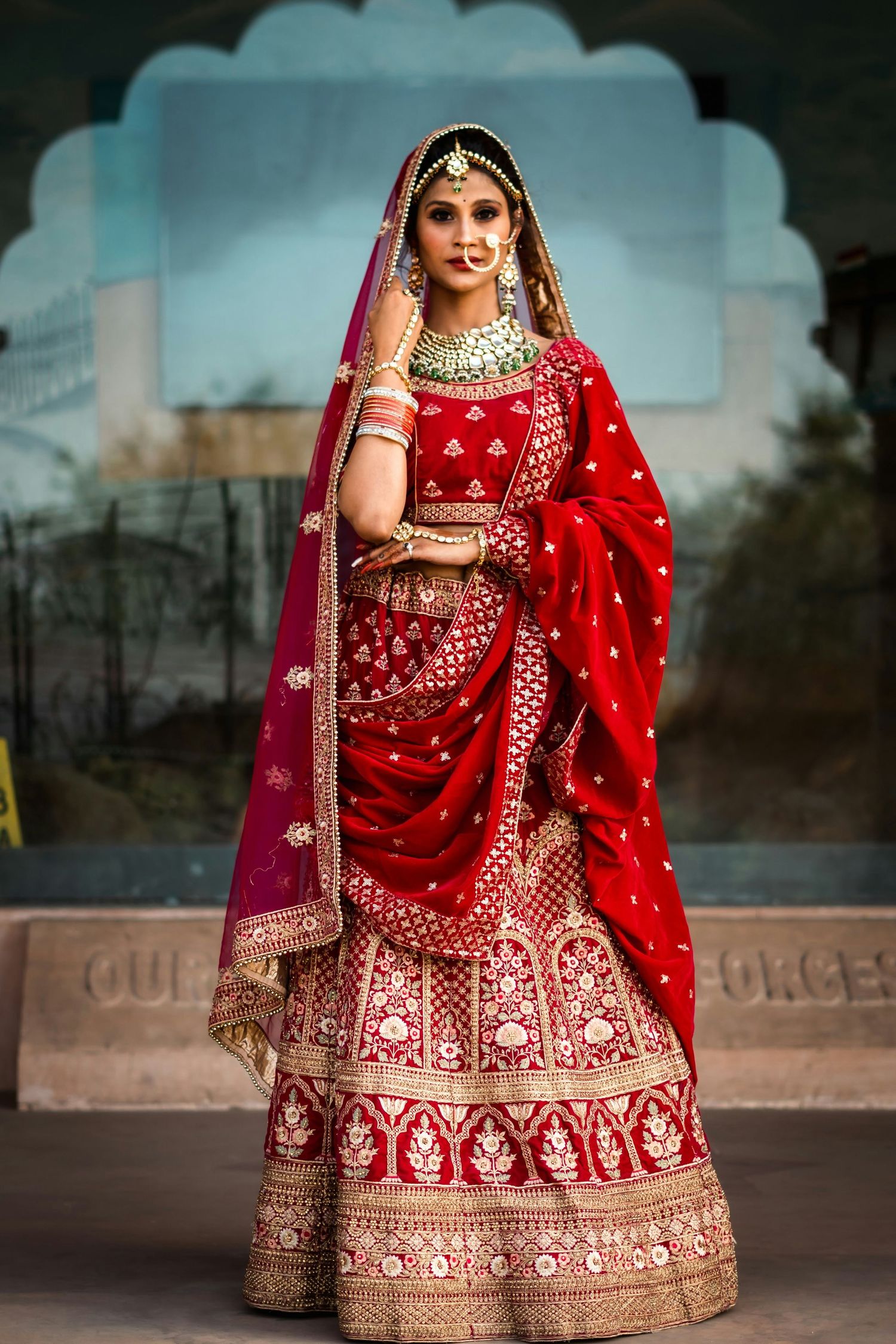 Indian bride in ornate red and gold lehenga with traditional bridal jewelry.