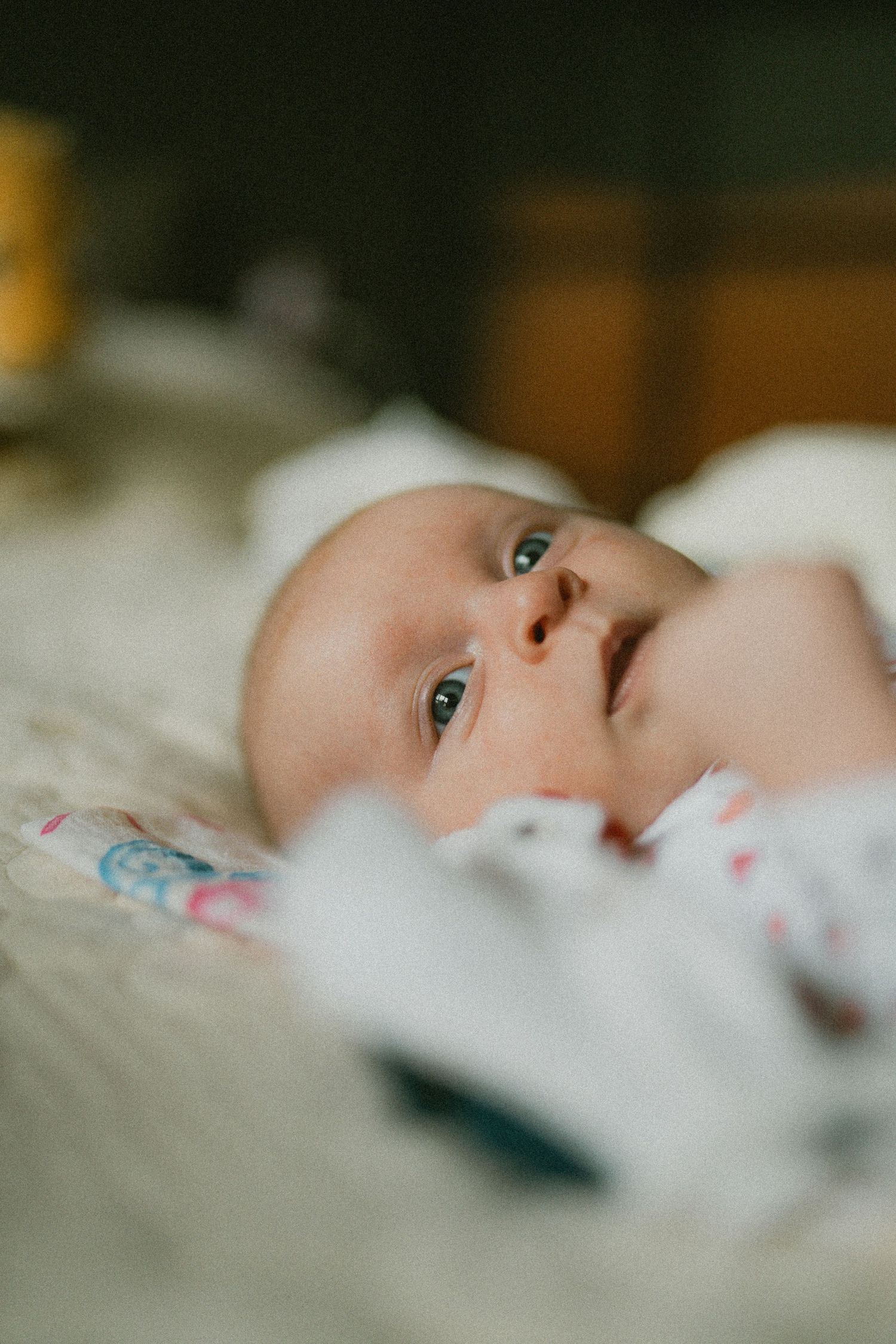 Newborn baby with blue eyes lying on soft white blanket looking upward.