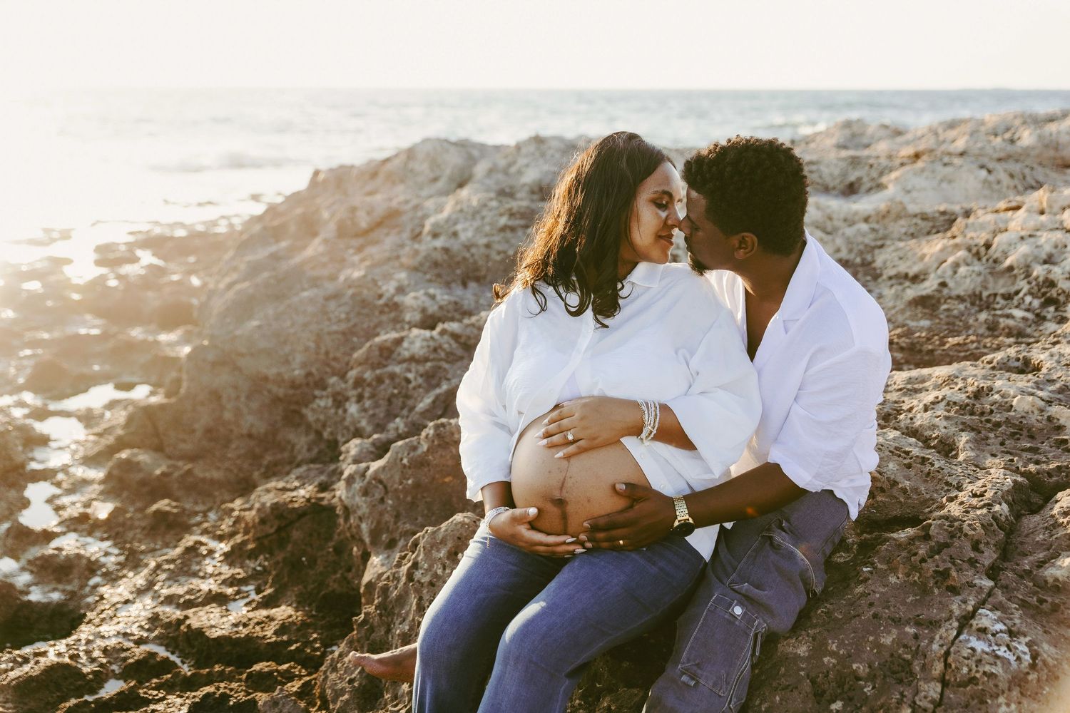 Ottawa maternity photoshoot couple sitting on rocky shore at sunset - R&B AuraCapture