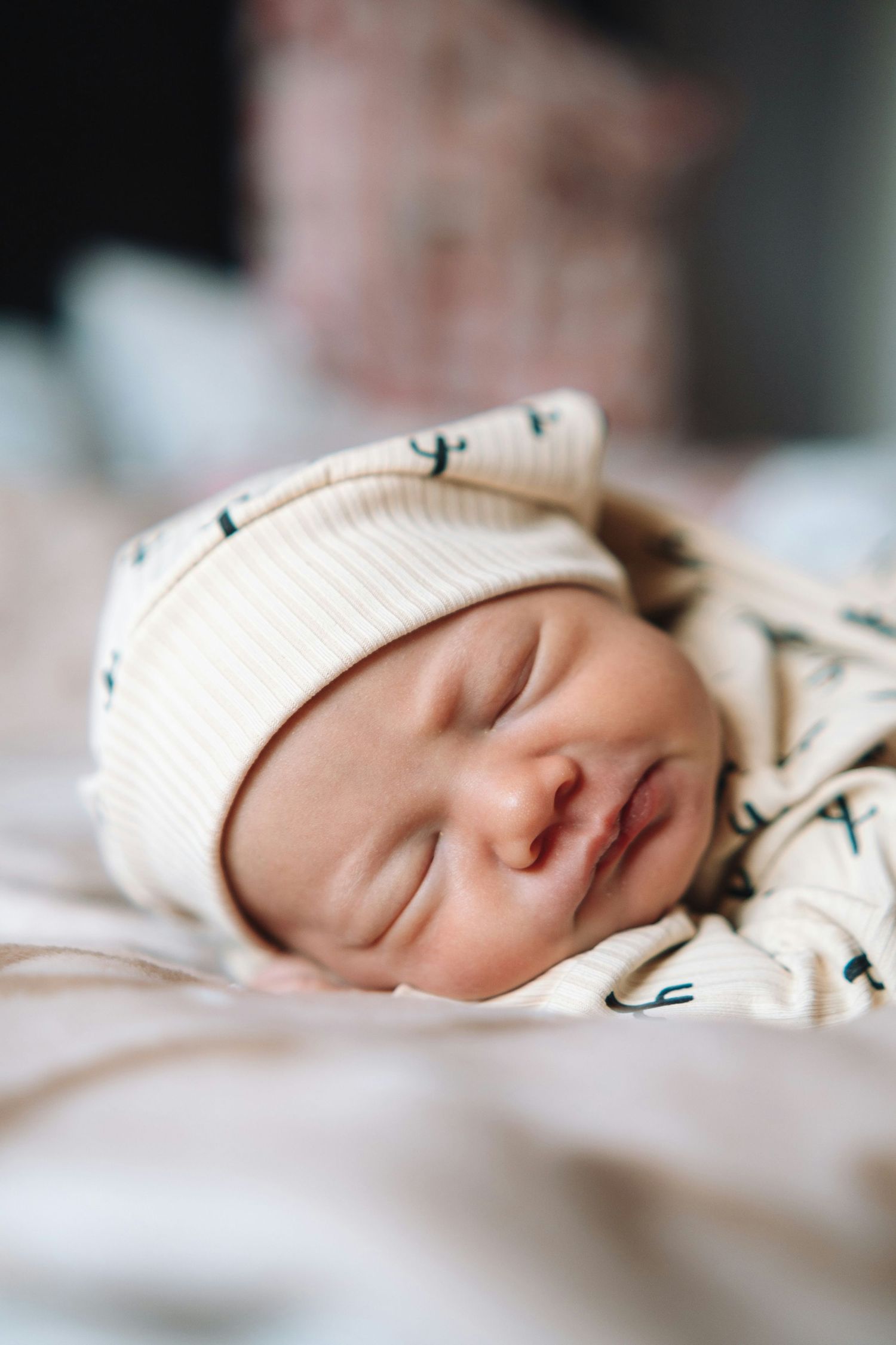 Close-up of a sleeping newborn wearing a white cactus-print outfit and matching knotted hospital hat.