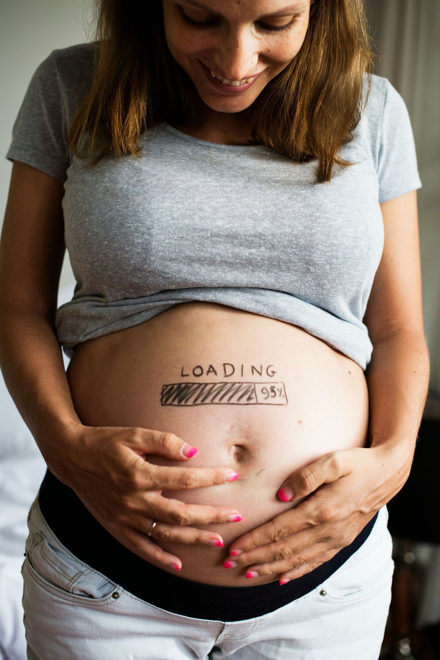 Smiling pregnant woman with loading bar drawn on belly at 95 percent.