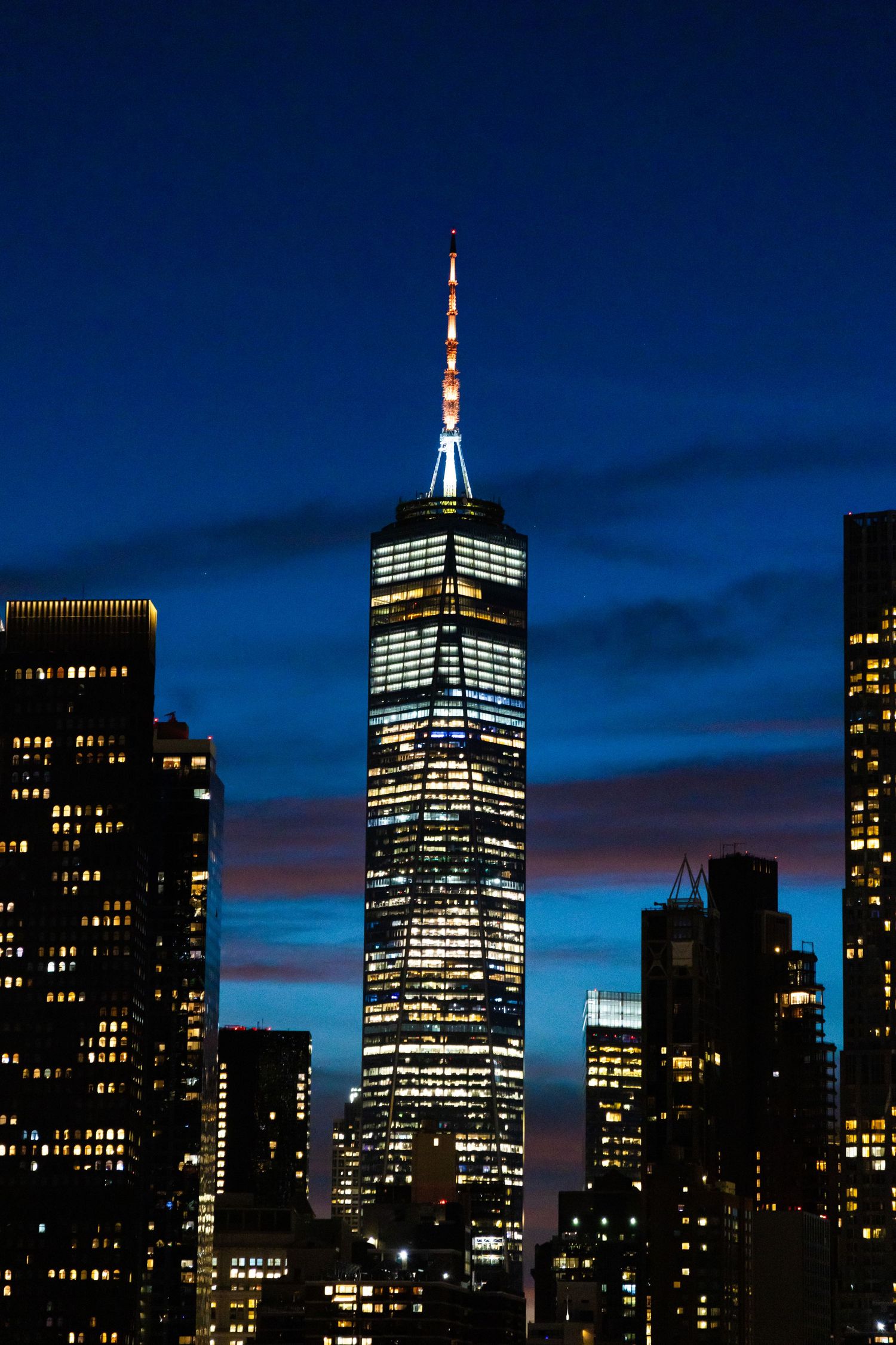 One World Trade Center illuminated at dusk against a blue sky in New York City skyline.
