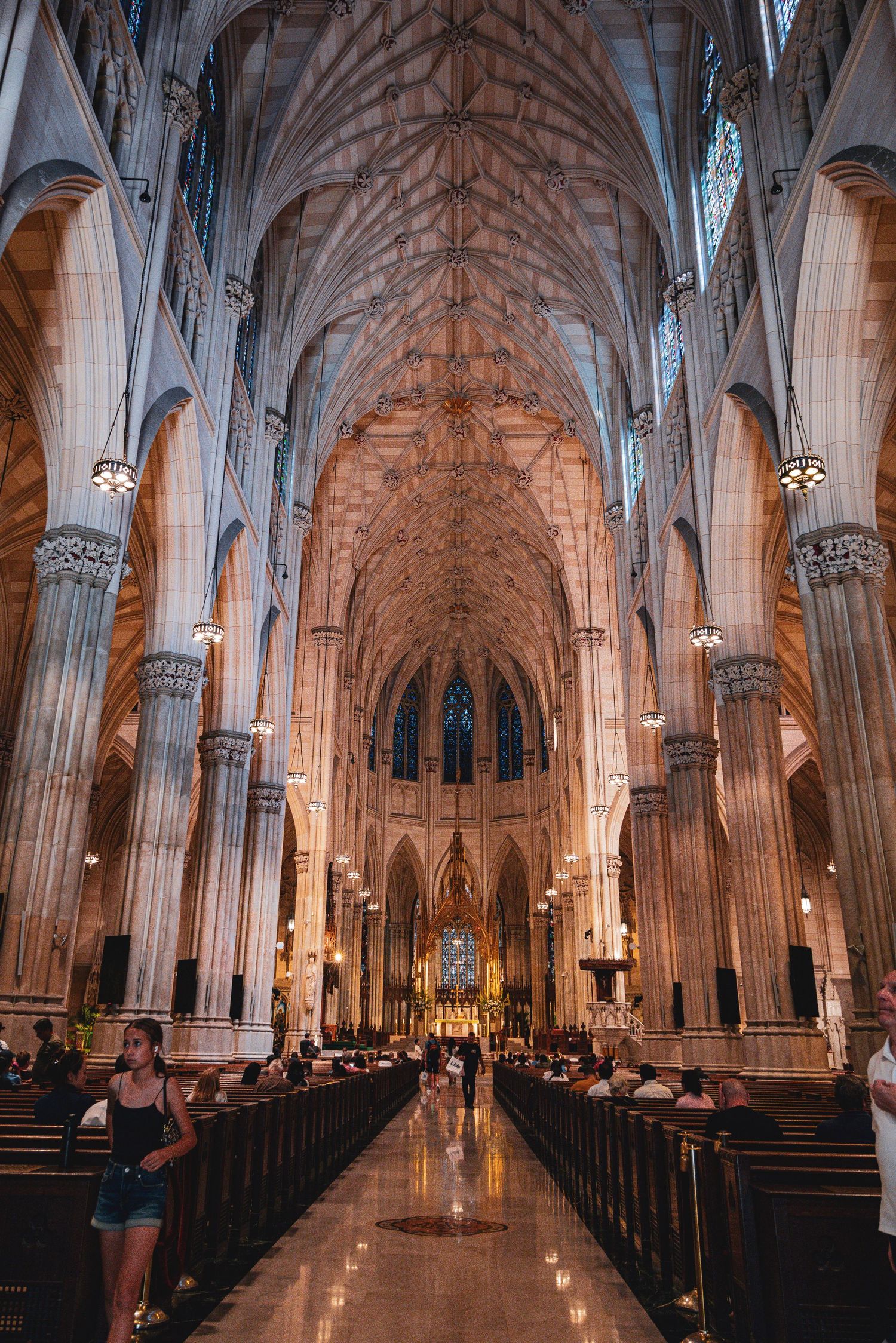 Interior of St. Patrick's Cathedral in NYC, featuring Gothic arches, vaulted ceilings, stained glass, and wooden pews.
