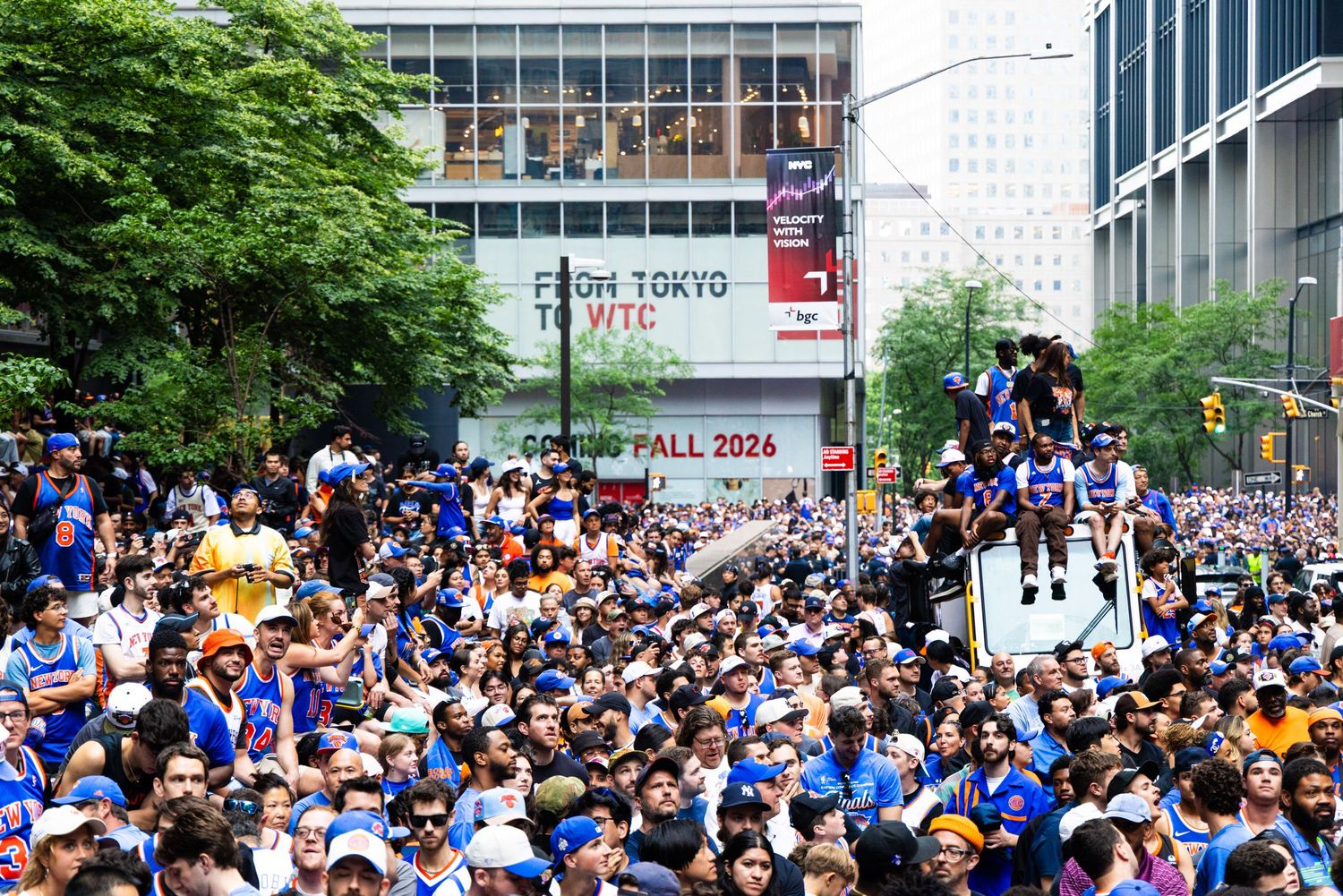 Massive crowd fills city street during a sports championship parade with fans in blue jerseys and a banner reading Coming Fall 2026.
