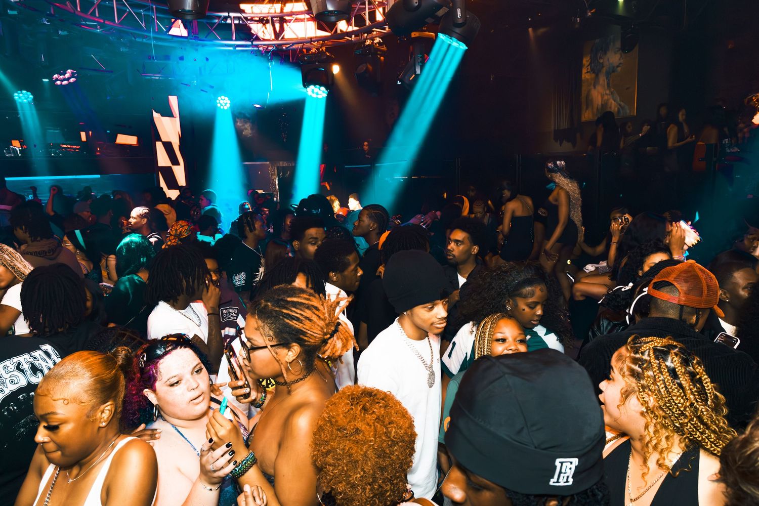 Crowded nightclub dance floor with diverse partygoers dancing under blue and green stage lights.