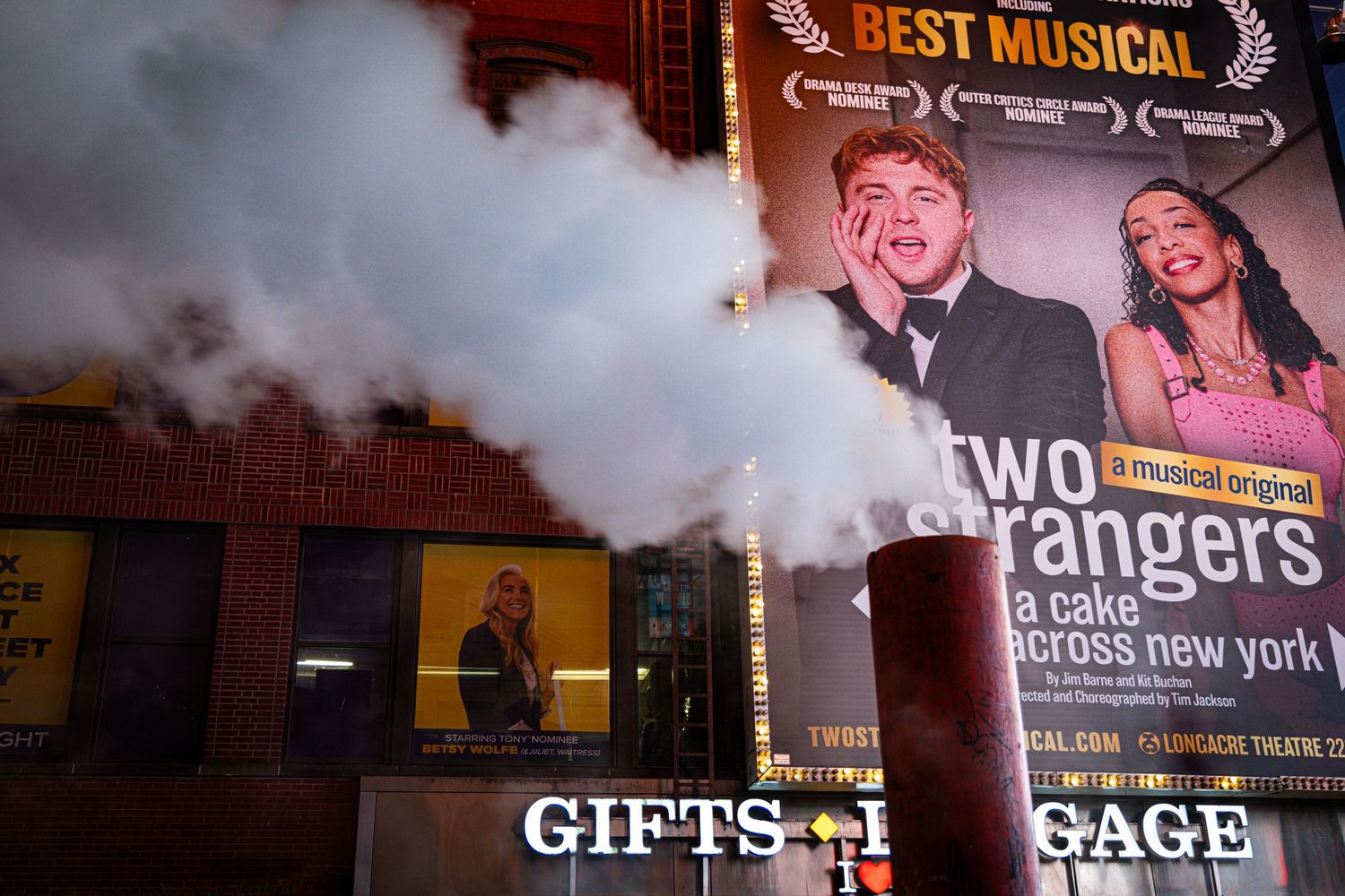 Broadway musical Two Strangers billboard in Times Square with steam rising from street vents at night.