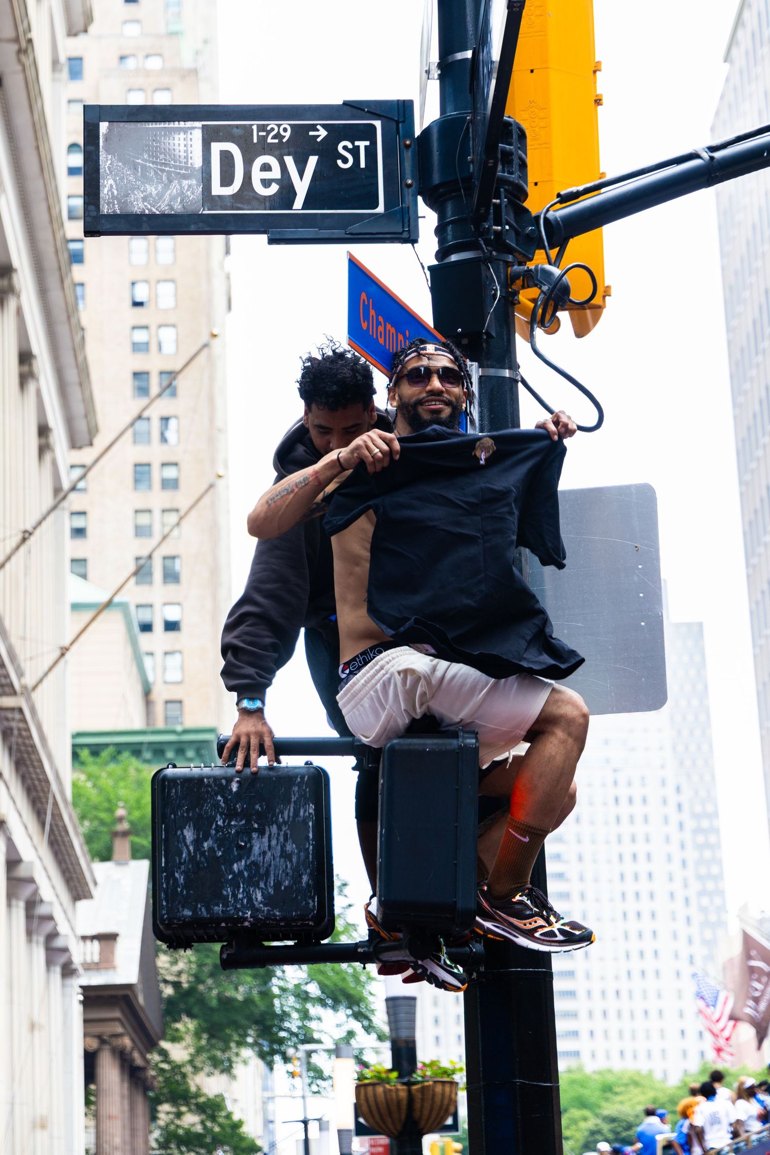 Two men climbing a street sign pole at Dey St in New York City during a street celebration.